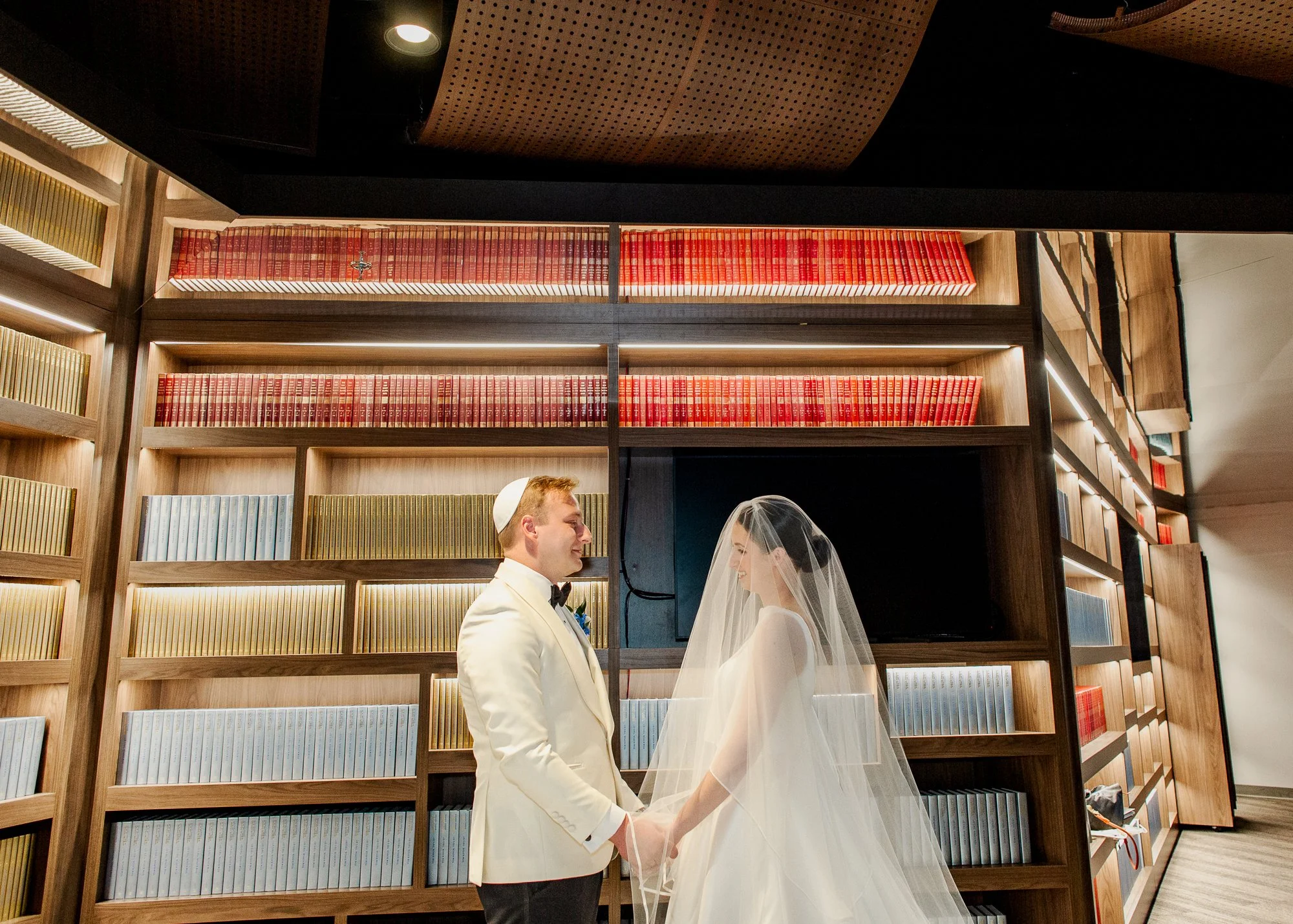 Sarah and Owen taking wedding portraits in the Temple Shir Shalom library