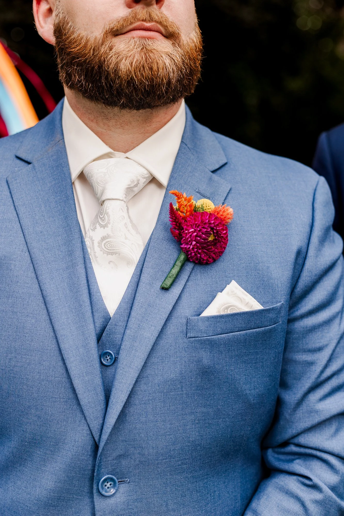 close of rainbow bouttonniere pinned on a mediium blue suit with white paisley tie