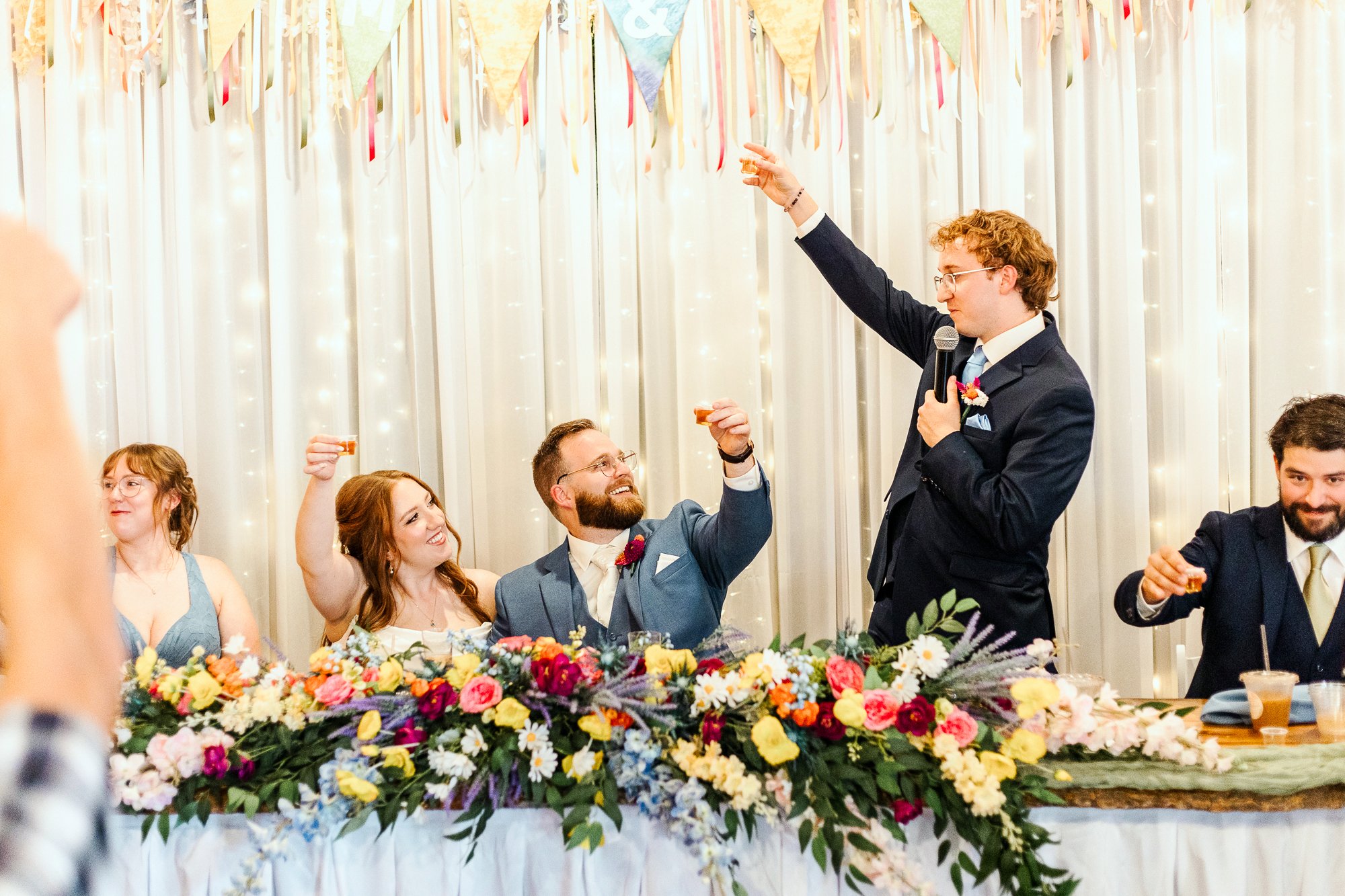 wide shot of brother of the bride toasting to the bride and groom at head table
