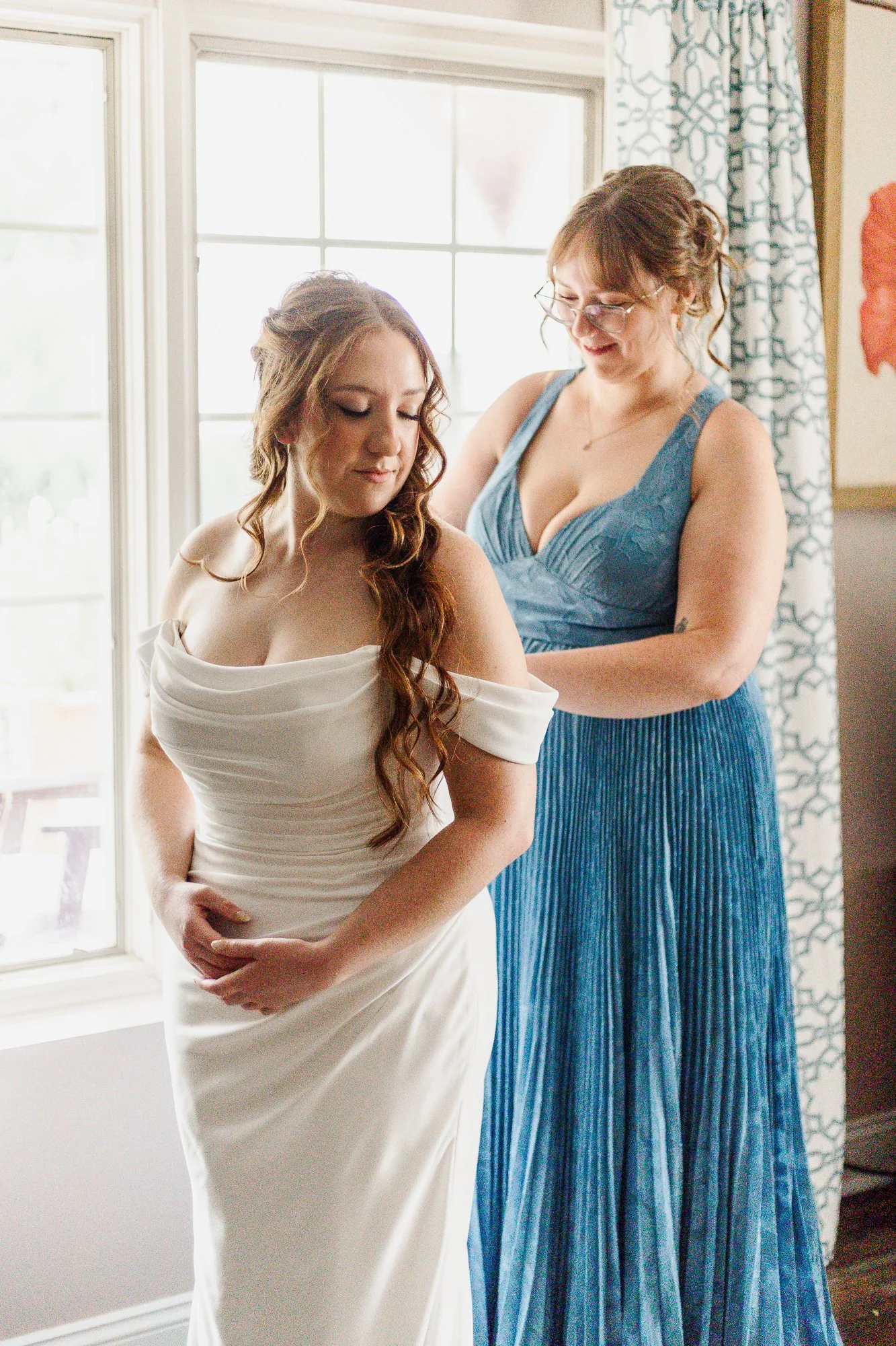 Sister in blue dress helping bride zip up her dress at Bloom and Bower in Risingsun, Ohio