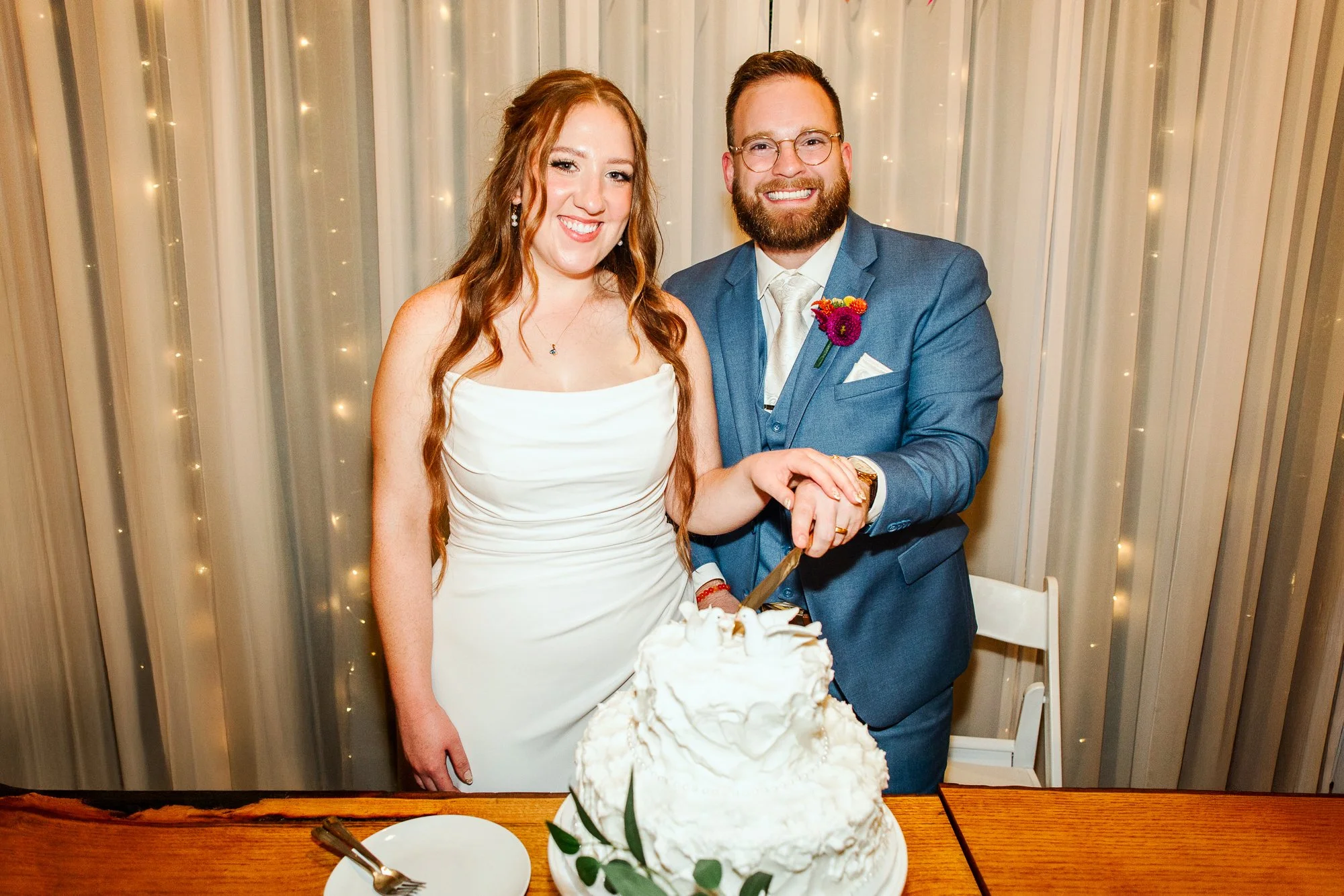close up of bride and groom smiling at the camera and cutting their wedding cake