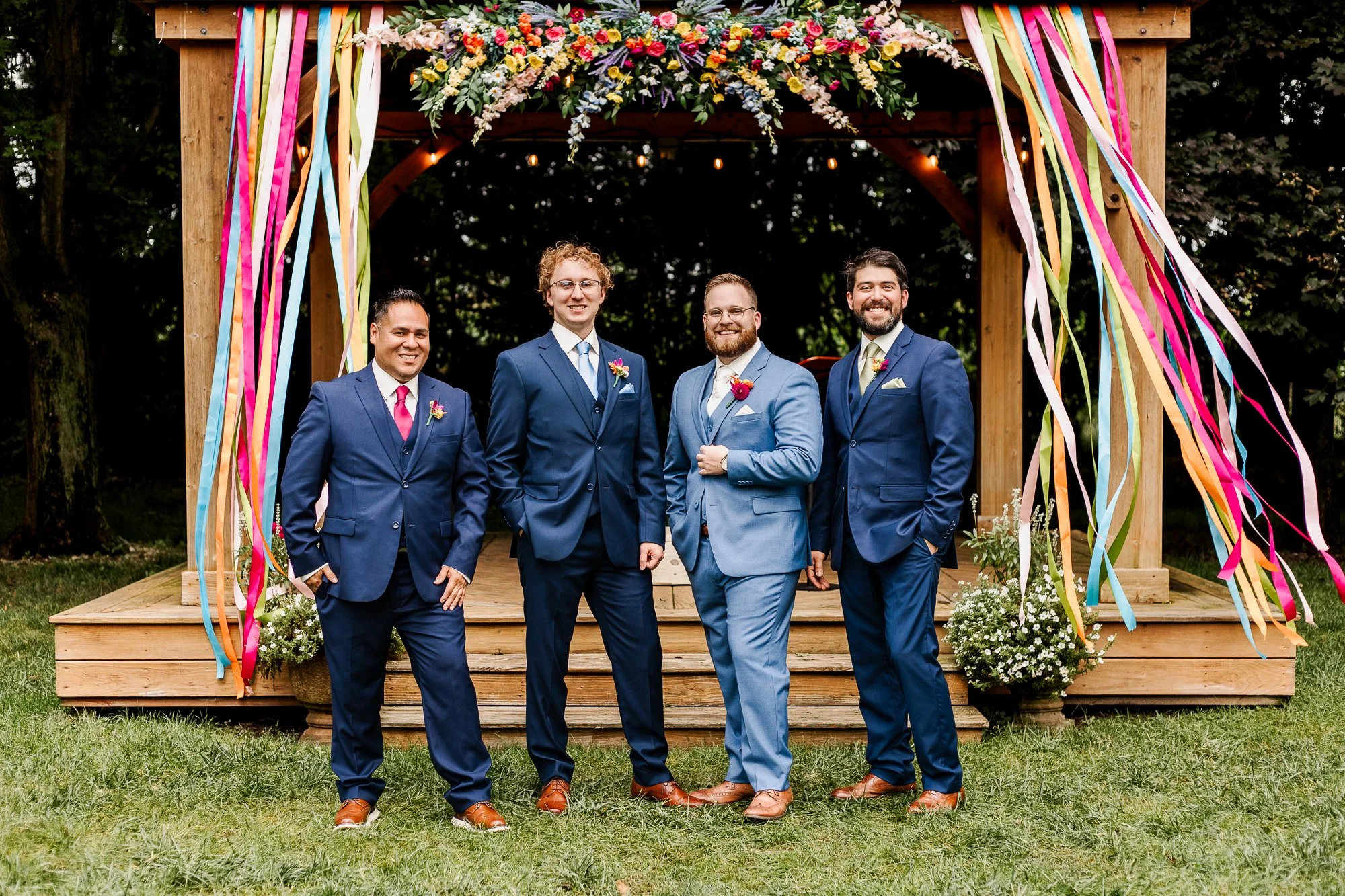 wide shot of groomsmen in blue suits posing in front of the rainbow-decorated gazebo at bloom and bower in rising sun ohio