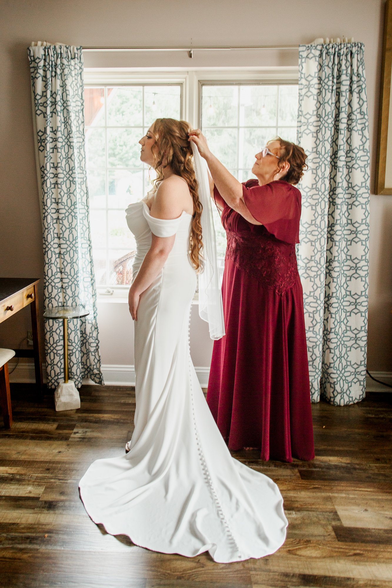 Full length photo of mom putting veil in bride's hair