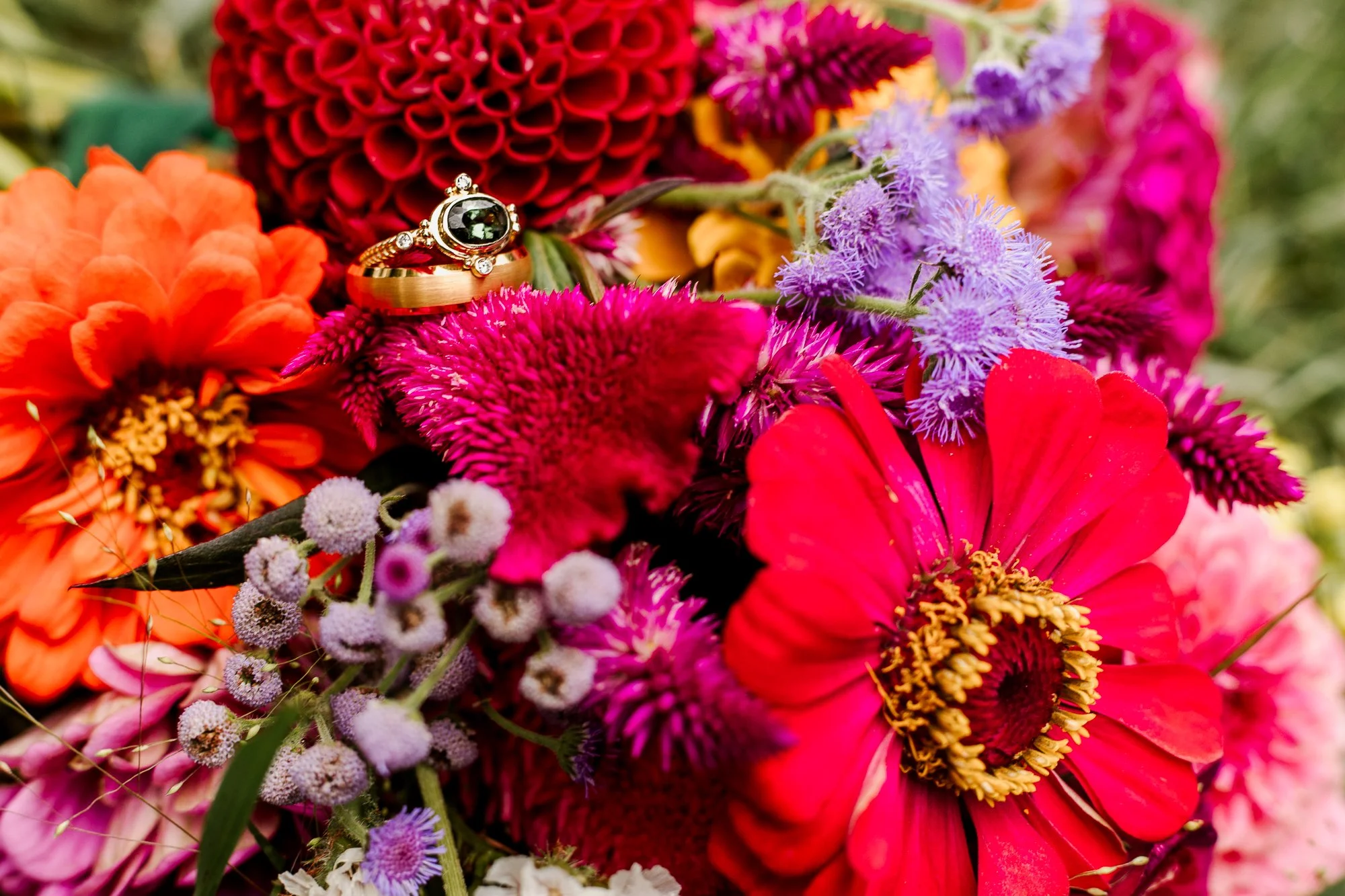 Close up of bride and groom wedding rings sitting on rainbow colored wedding bouquet