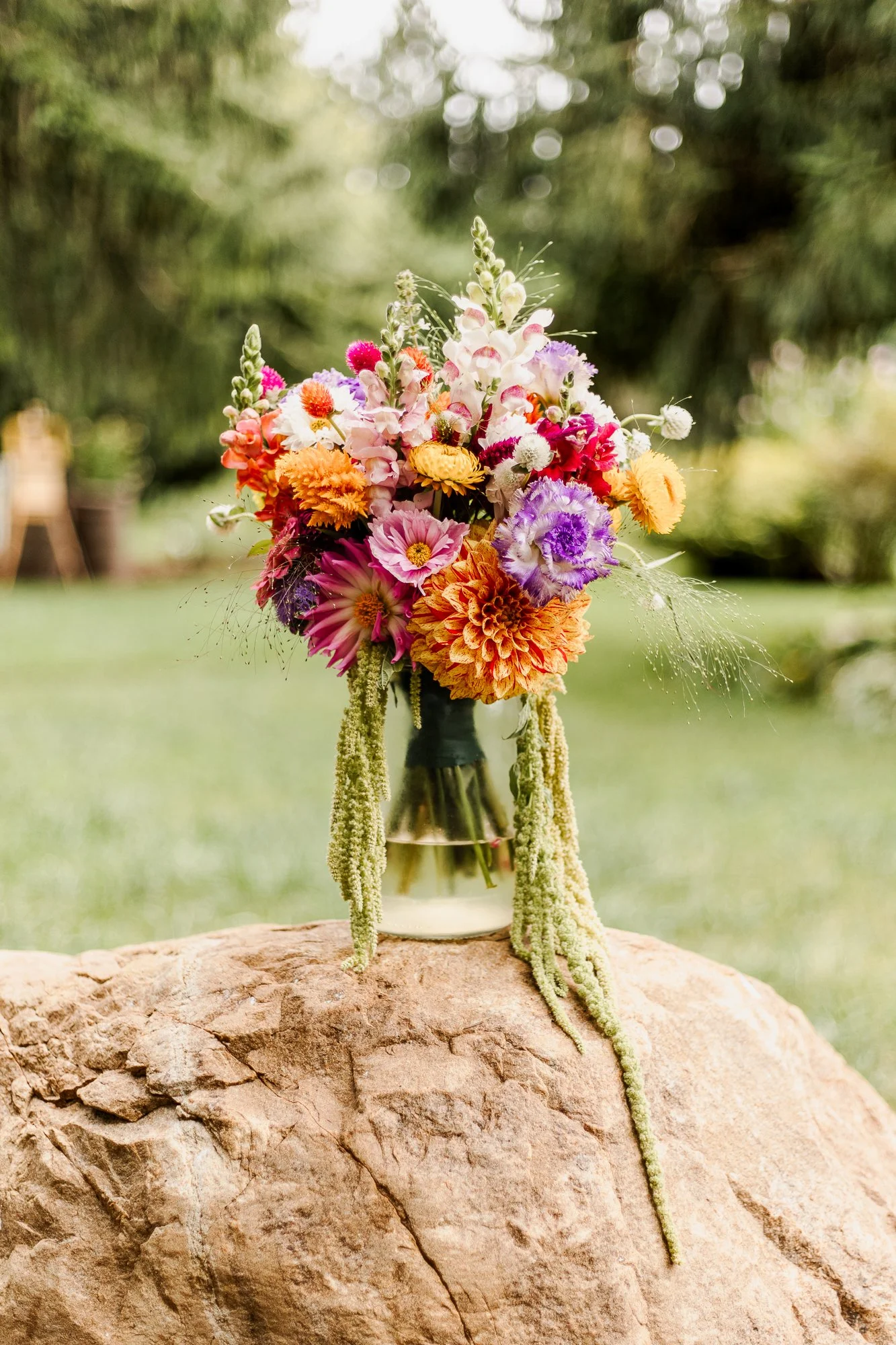 Rainbow colored bridal bouquet in a vase sitting on a rock