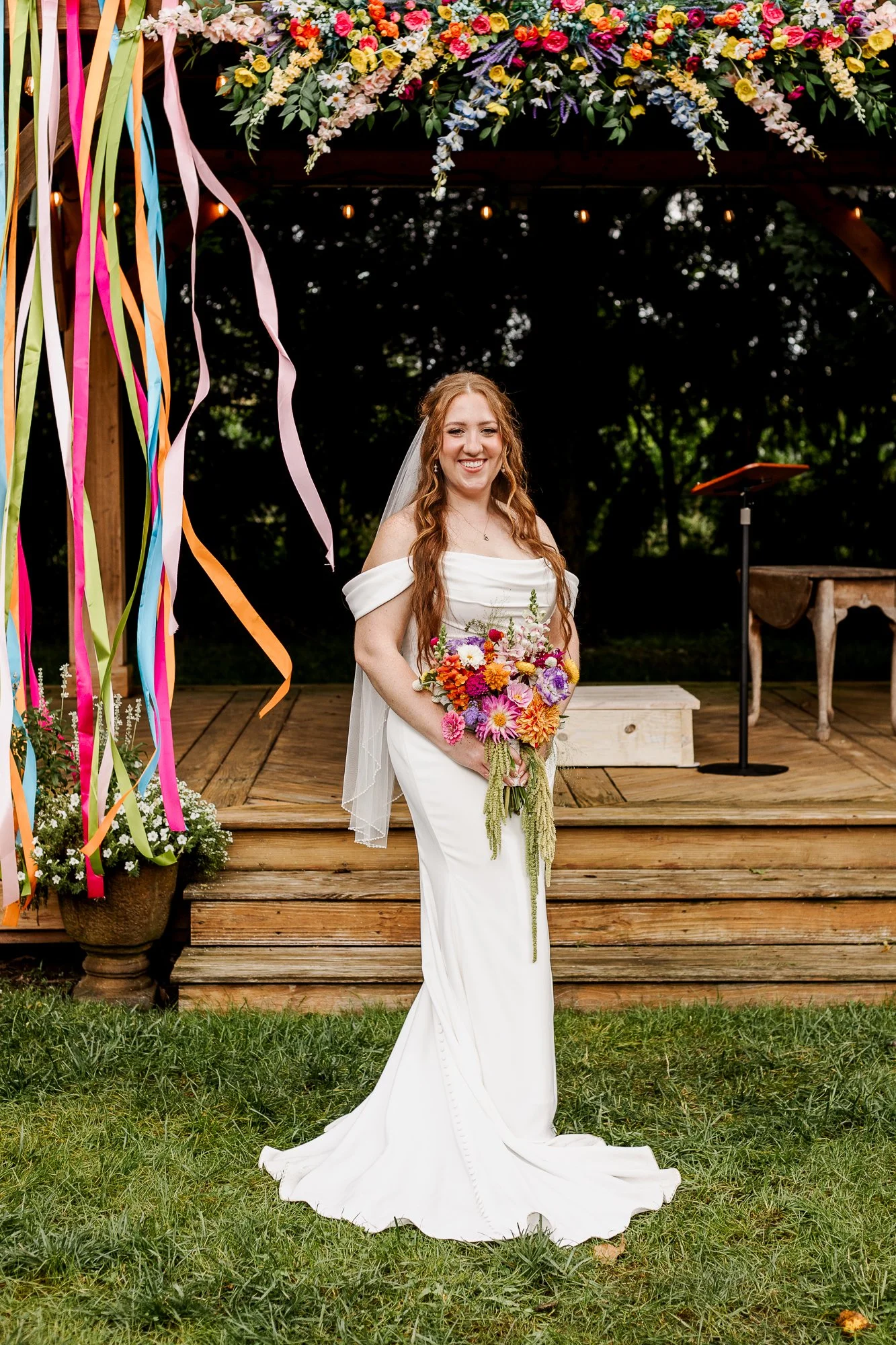 full length shot of bride holding a rainbow-colored bouquet in front of the gazebo ceremony site at bloom and bower in rising sun ohio