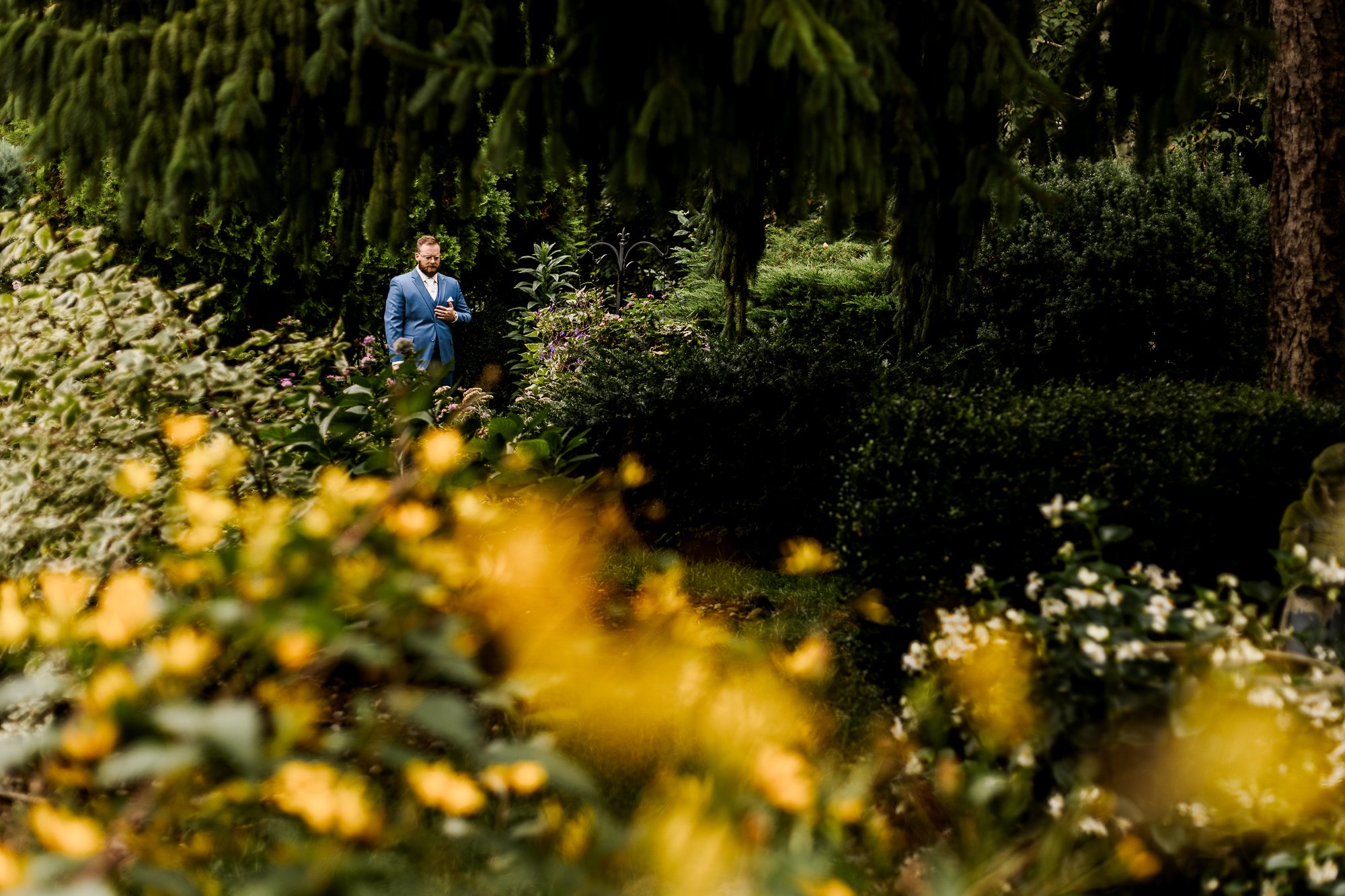Groom waiting in a flowering garden with his eyes closed for his first look with the bride at Bloom and Bower in Risingsun, Ohio
