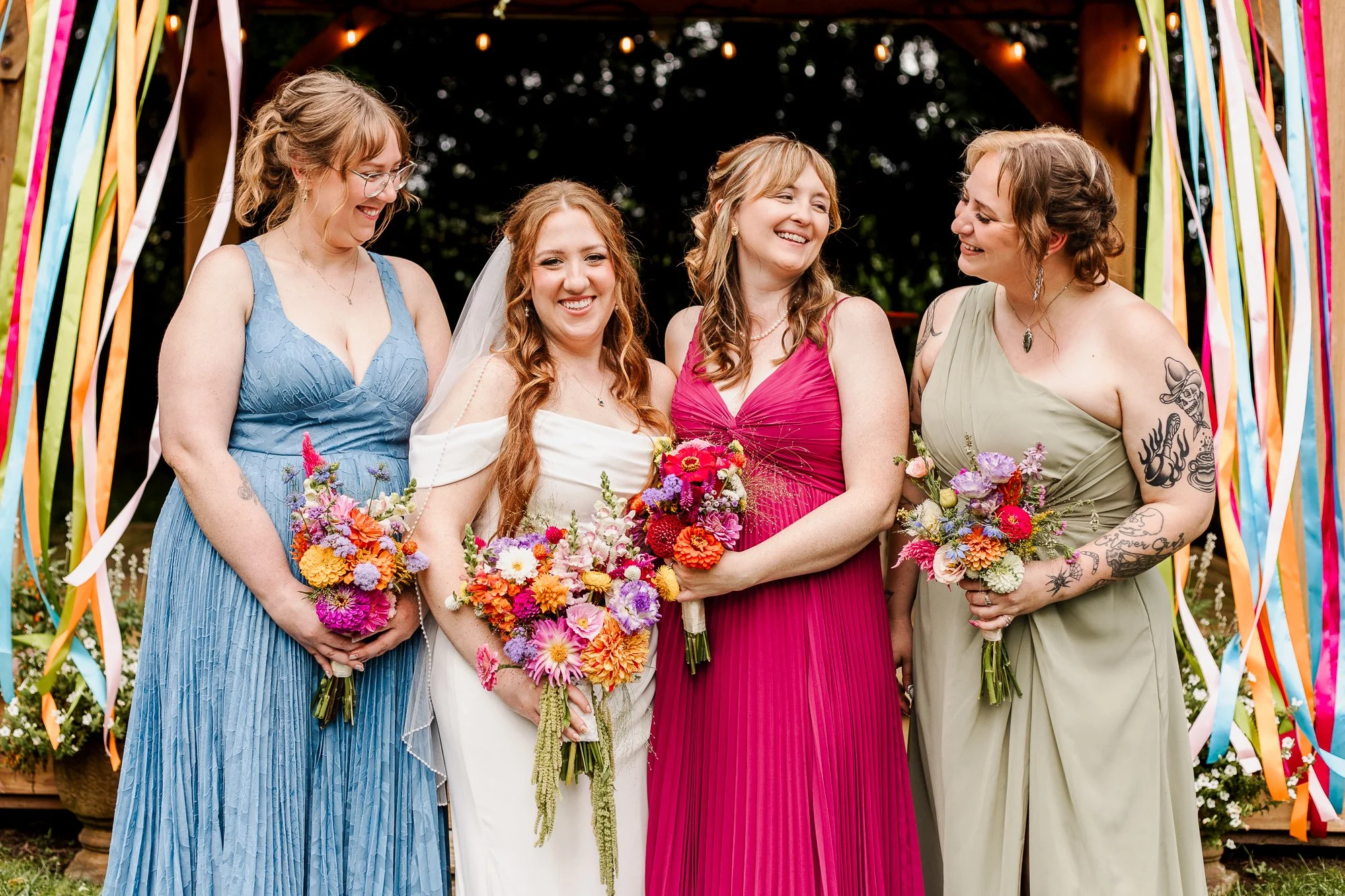close up of bridesmaids holding rainbow-colored bouquets and laughing with each other