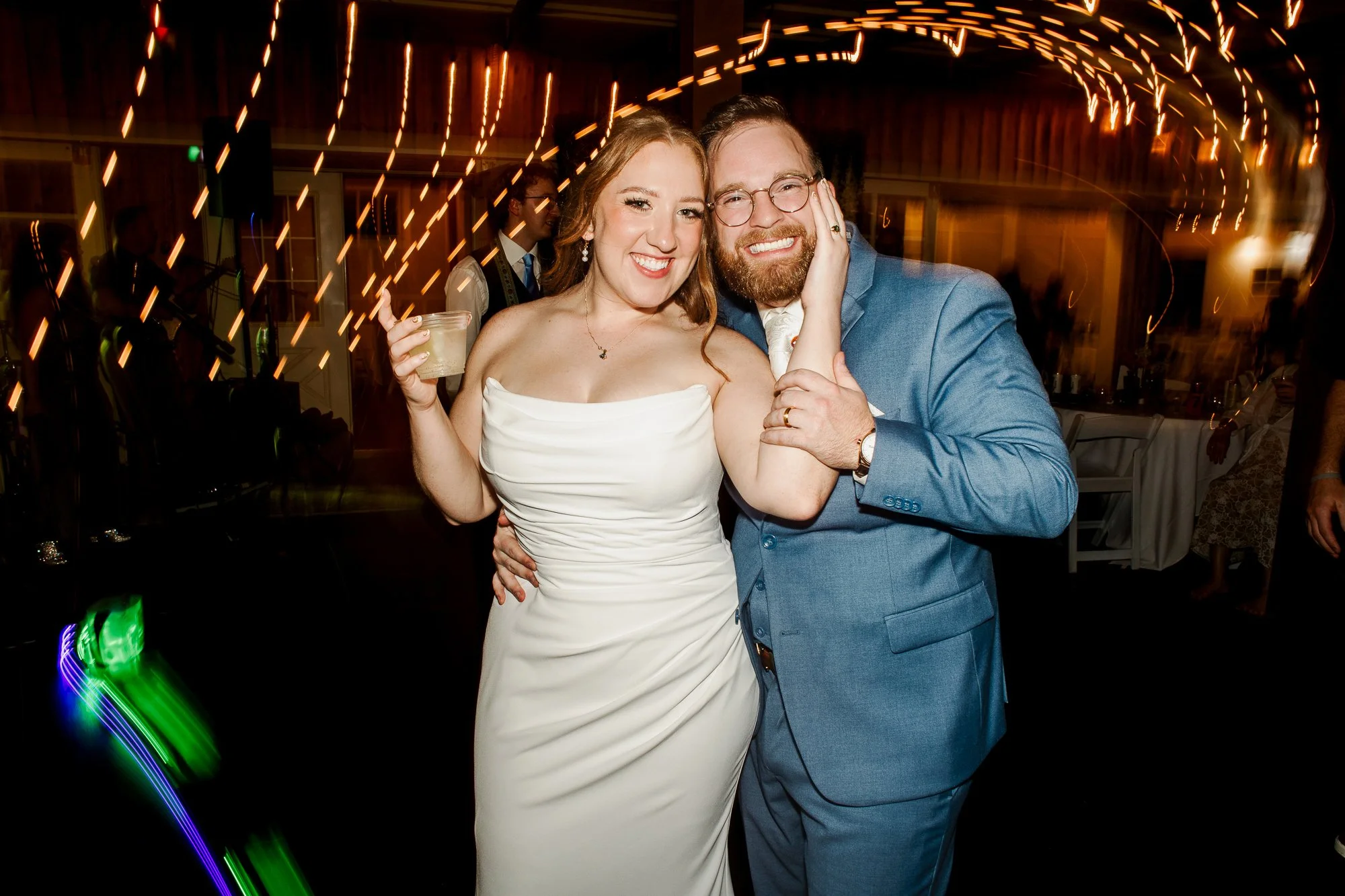 close up of bride and groom holding drinks and smiling at the camera on the dark dance floor of their wedding reception at bloom and bower in rising sun, ohio
