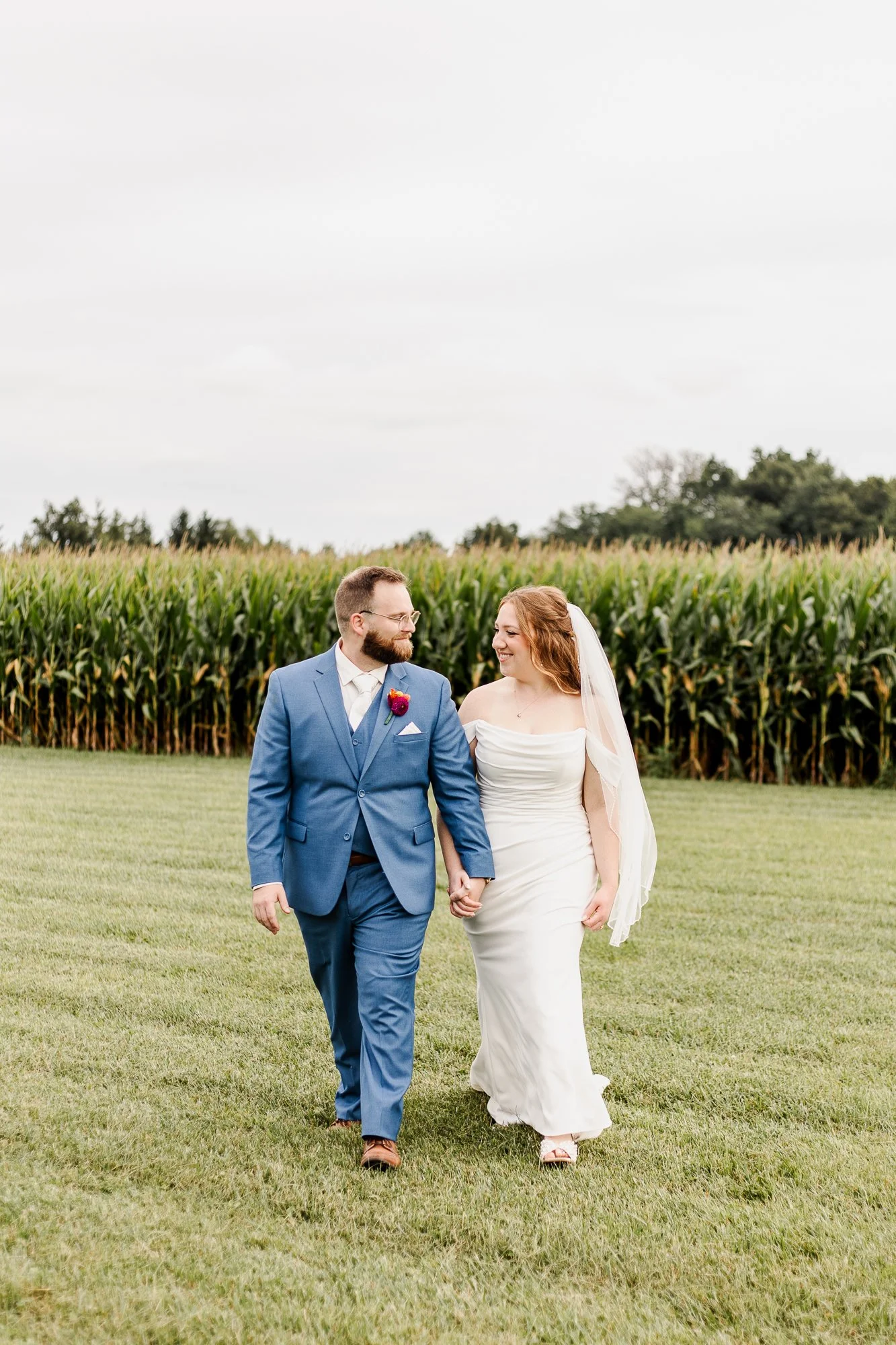 wide shot of bride and groom smiling and looking at each other and walking towards camera in a corn field