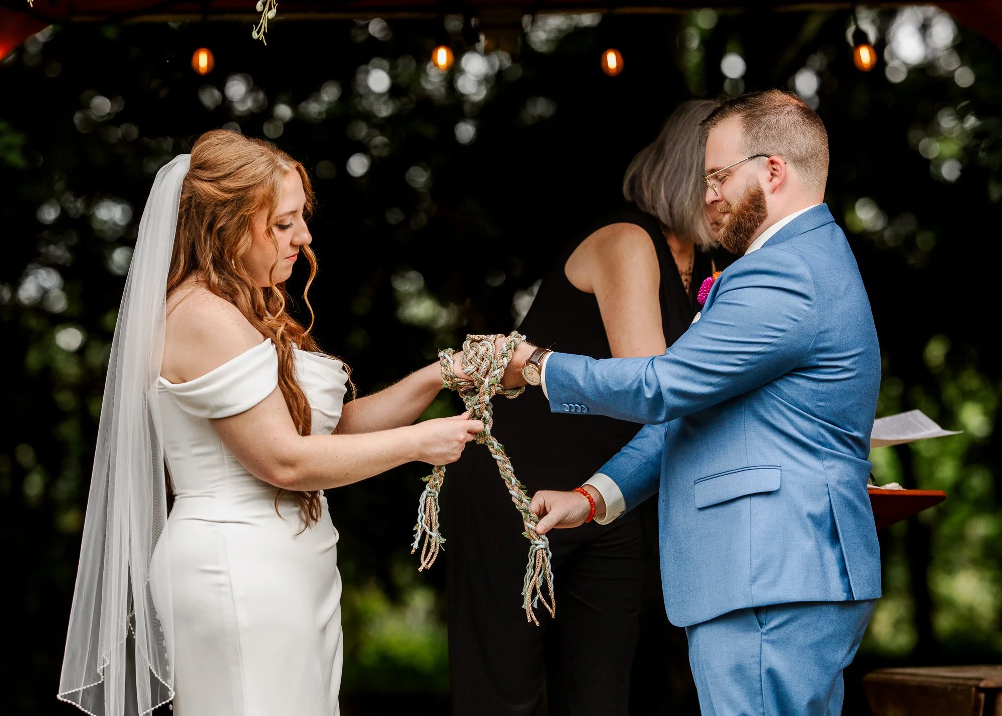 close up of bride and groom facing each other and performing handfasting tradition at the alter during ceremony