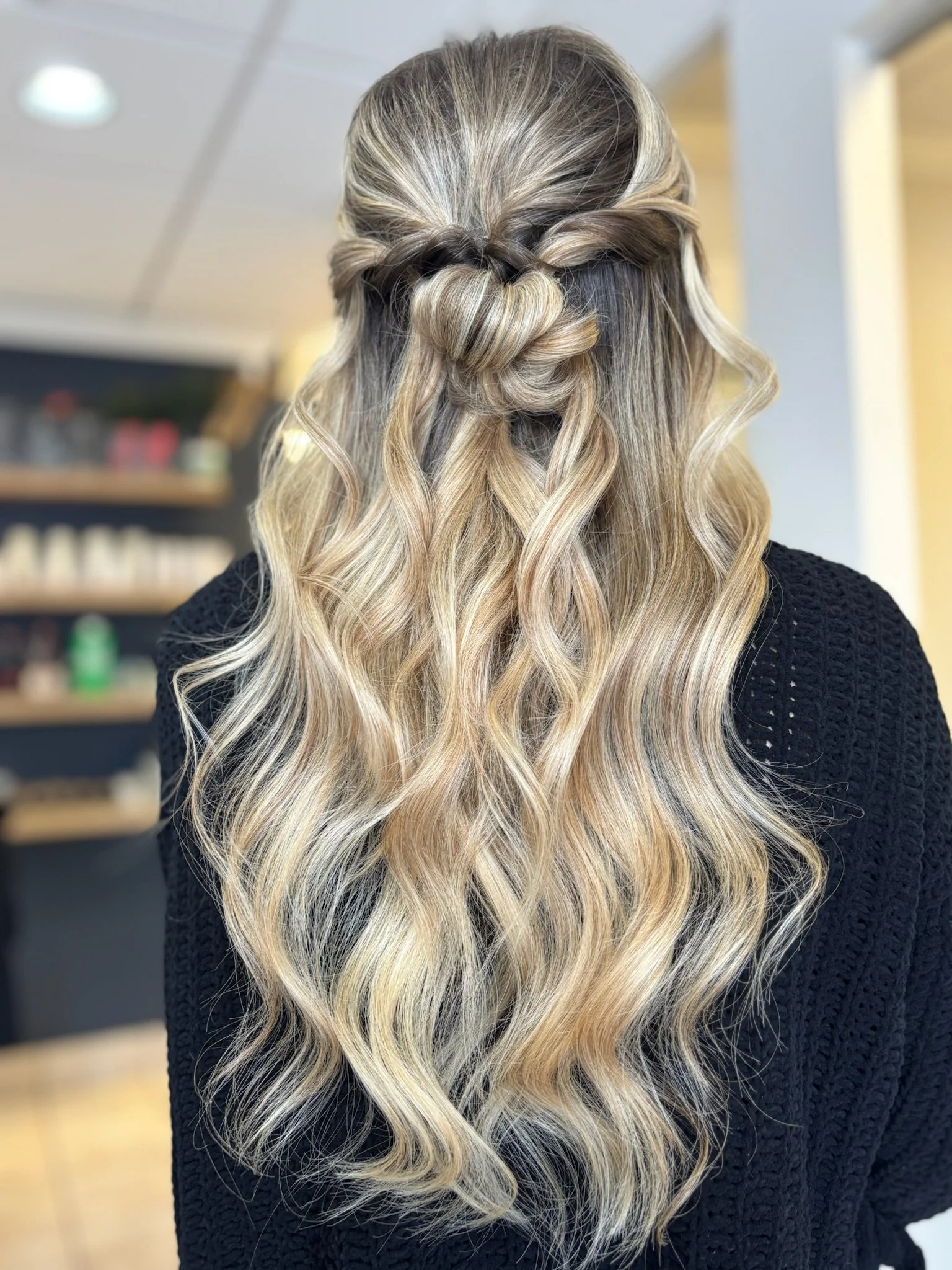 Back view of a woman with long, wavy blonde hair styled in a half-up, twisted braid.