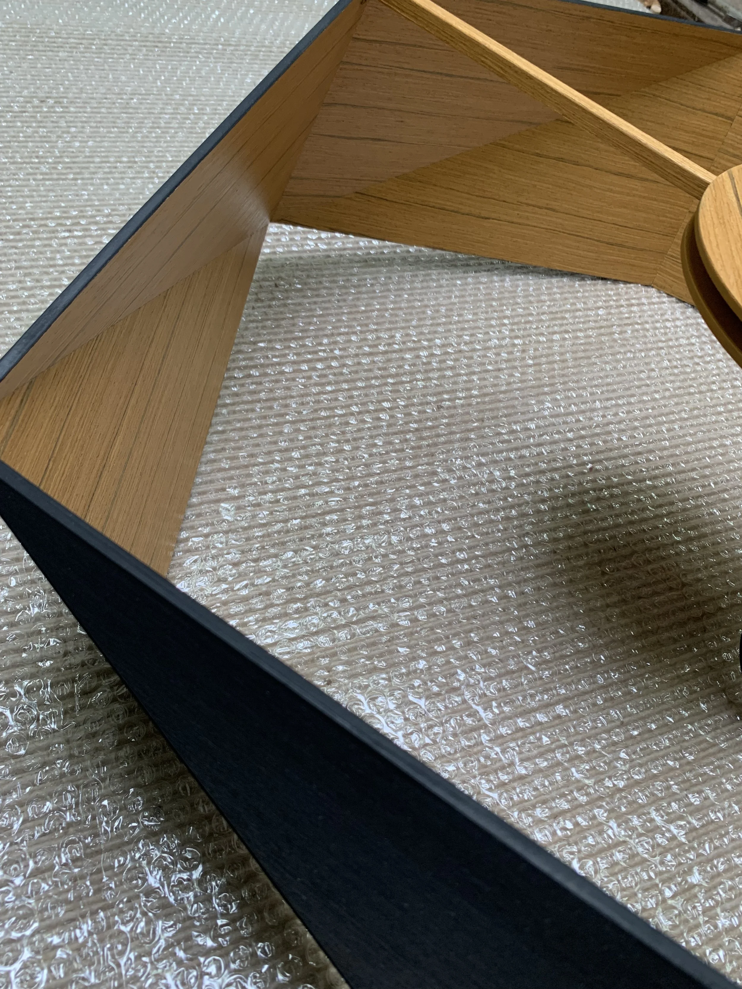 Close-up of a wooden table with a black frame and a transparent glass top, sitting on a textured beige carpet.