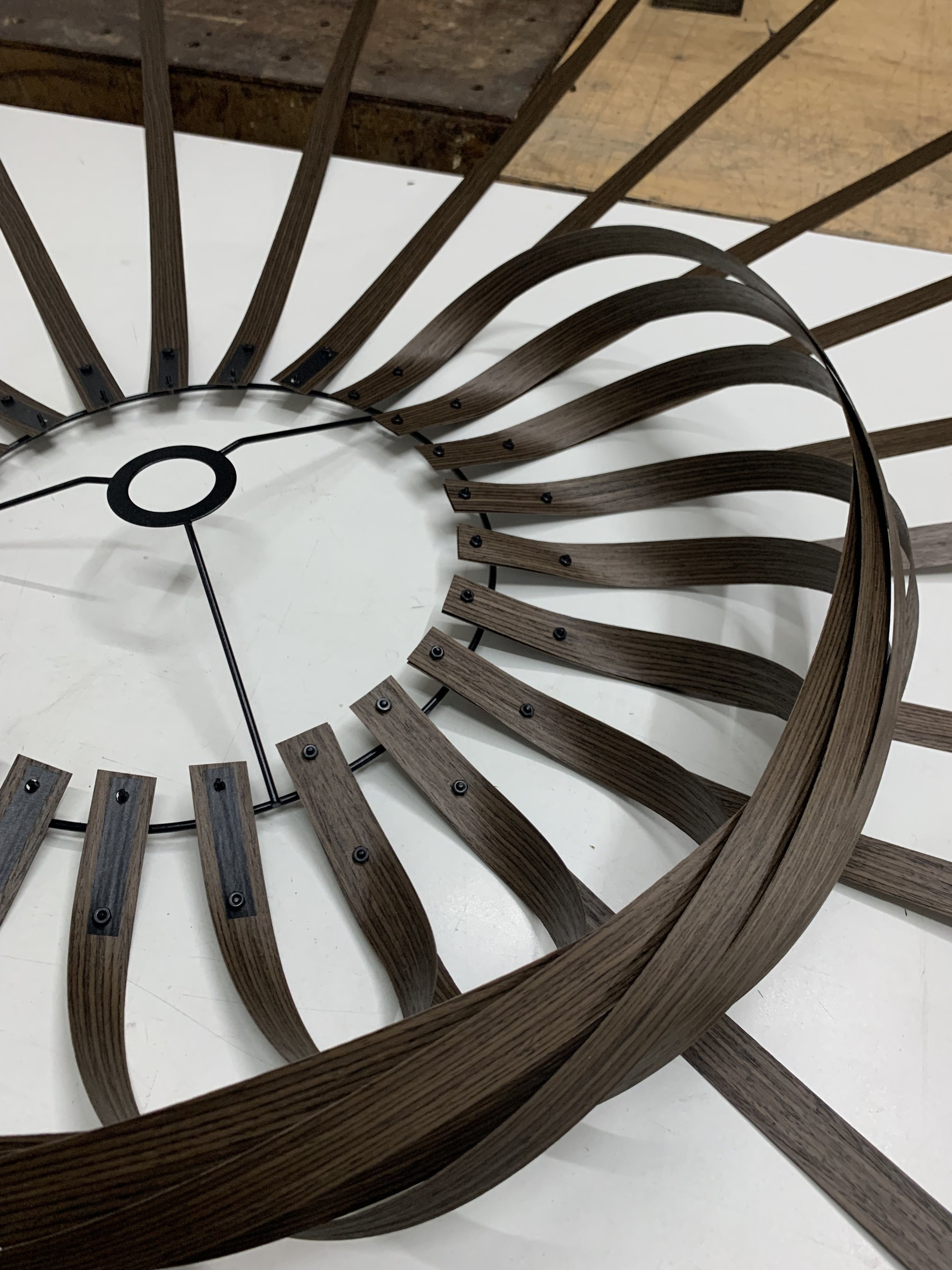 Close-up of a modern, decorative wall clock with a circular design, featuring spiral-shaped wooden strips radiating outward from the center on a white background.