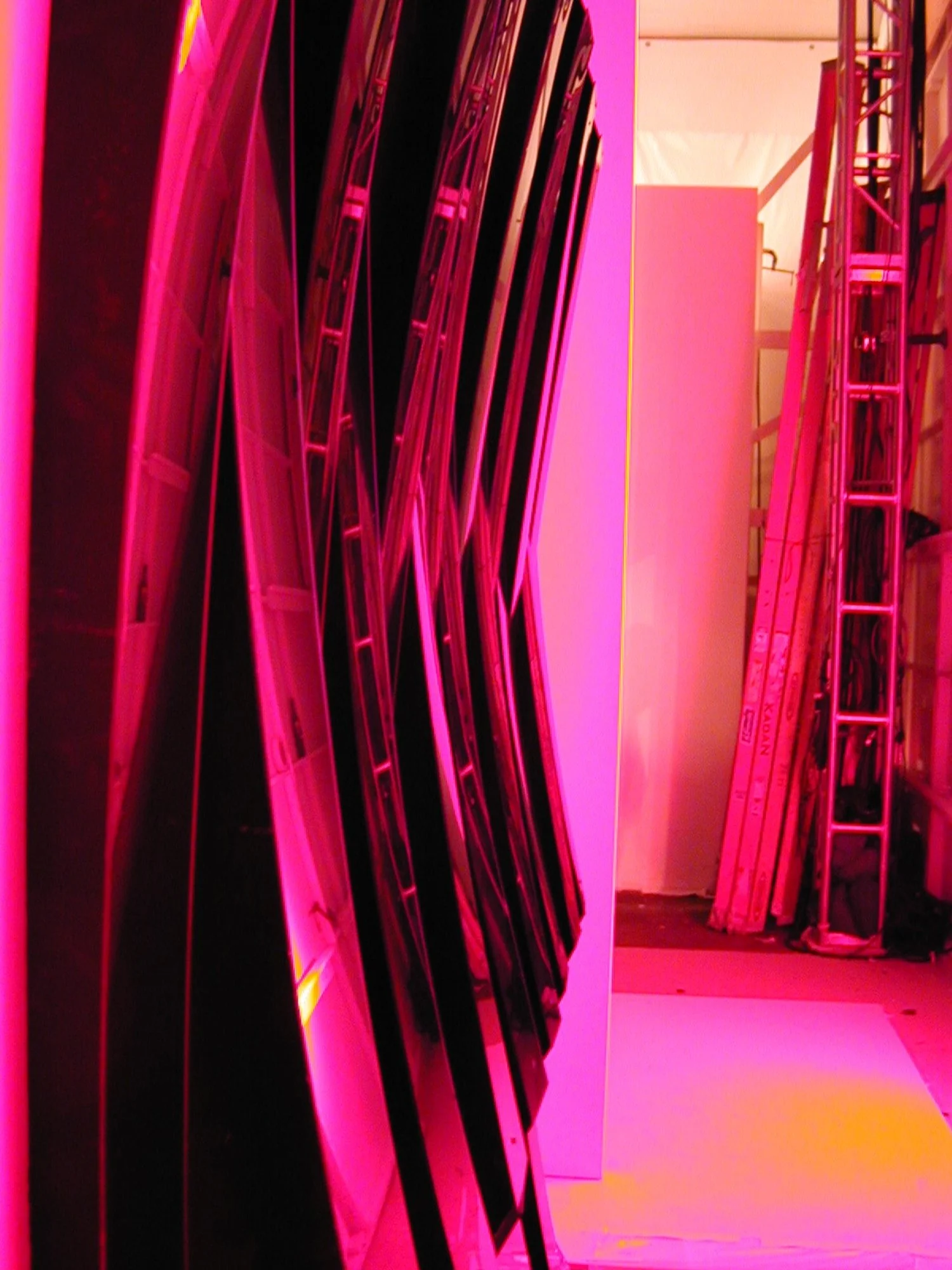 Stacks of black and pink LED screens or panels in a room with pink lighting, with scaffolding on the right side.