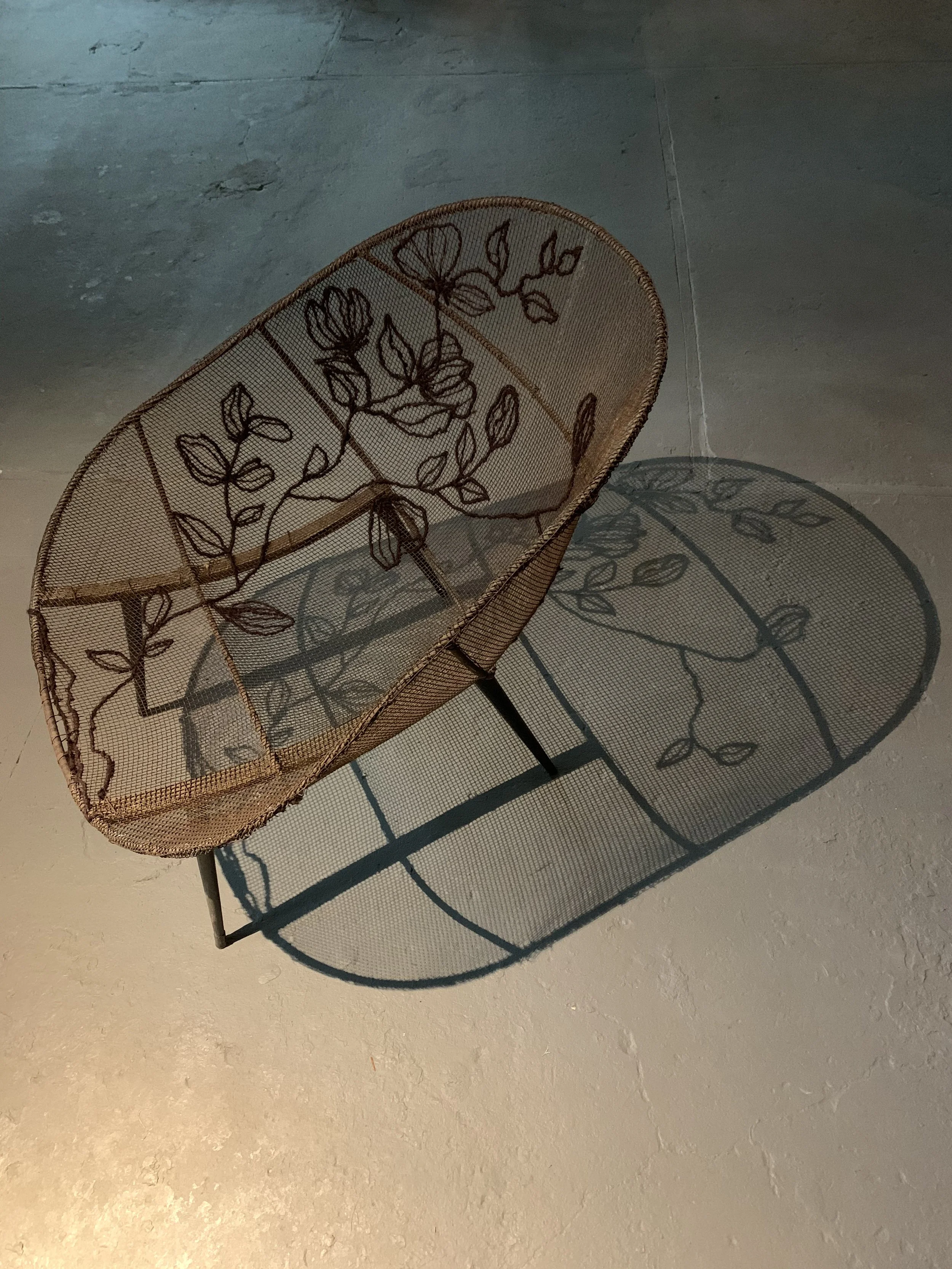 A woven hanging chair with a floral pattern cast a shadow on the ceiling.