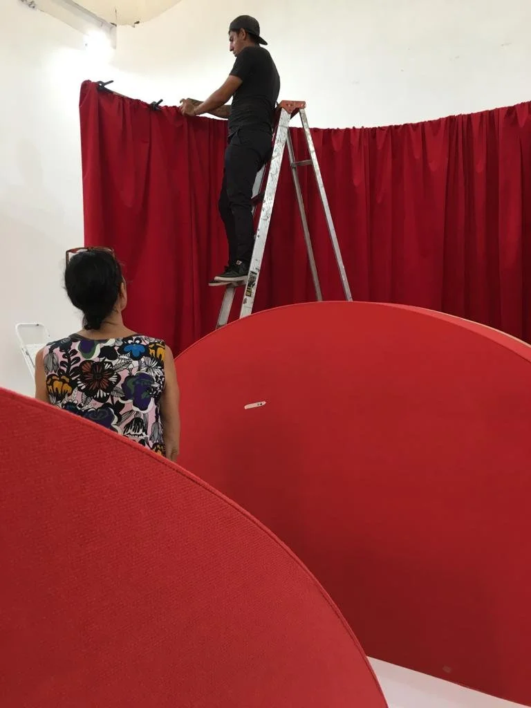 A man standing on a ladder adjusting red curtains, with a woman sitting nearby watching him.