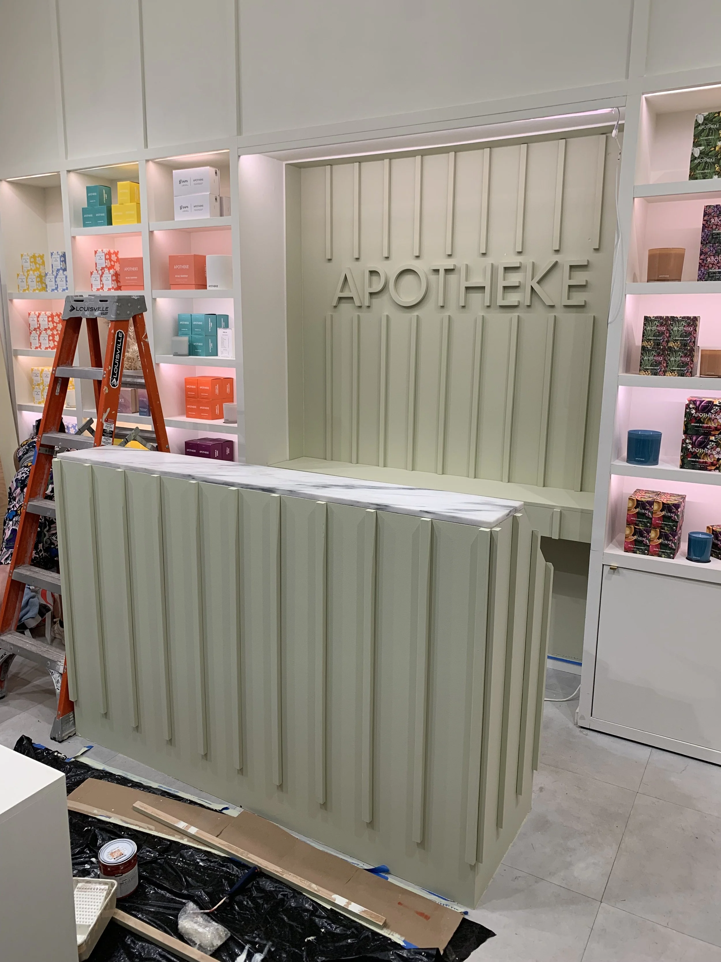 Interior of a pharmacy with shelving units and a counter, with a ladder nearby, and the word 'APOTHEKE' on the wall.