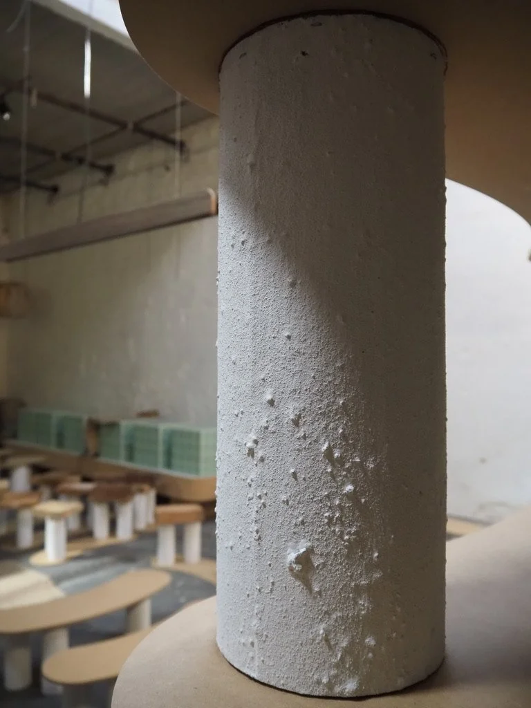 Close-up of a textured white cylindrical object, possibly in a workshop or industrial setting, with furniture and shelves in the background.
