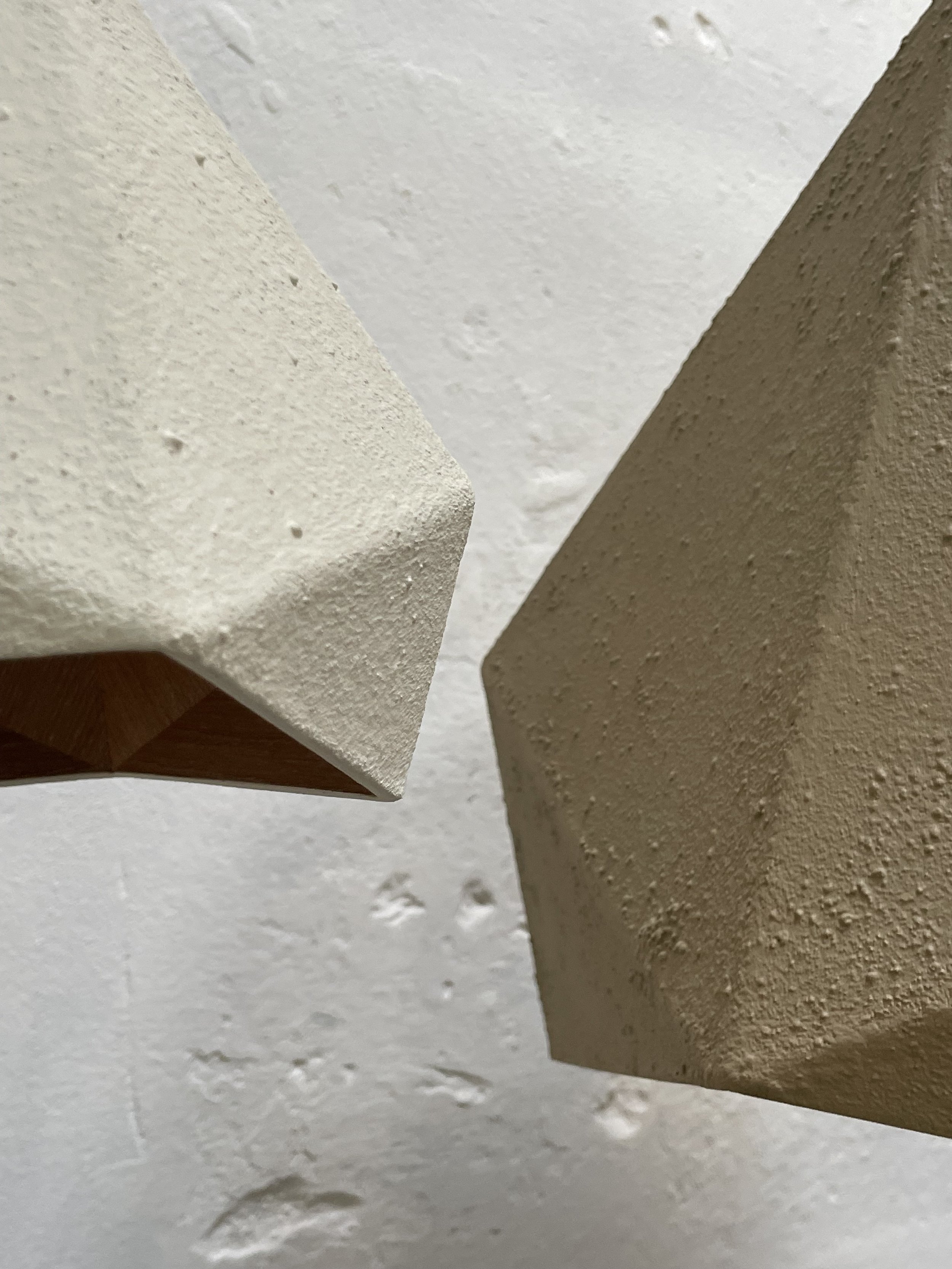 Close-up of two textured, angular objects in white and beige, set against a white wall with small indentations.