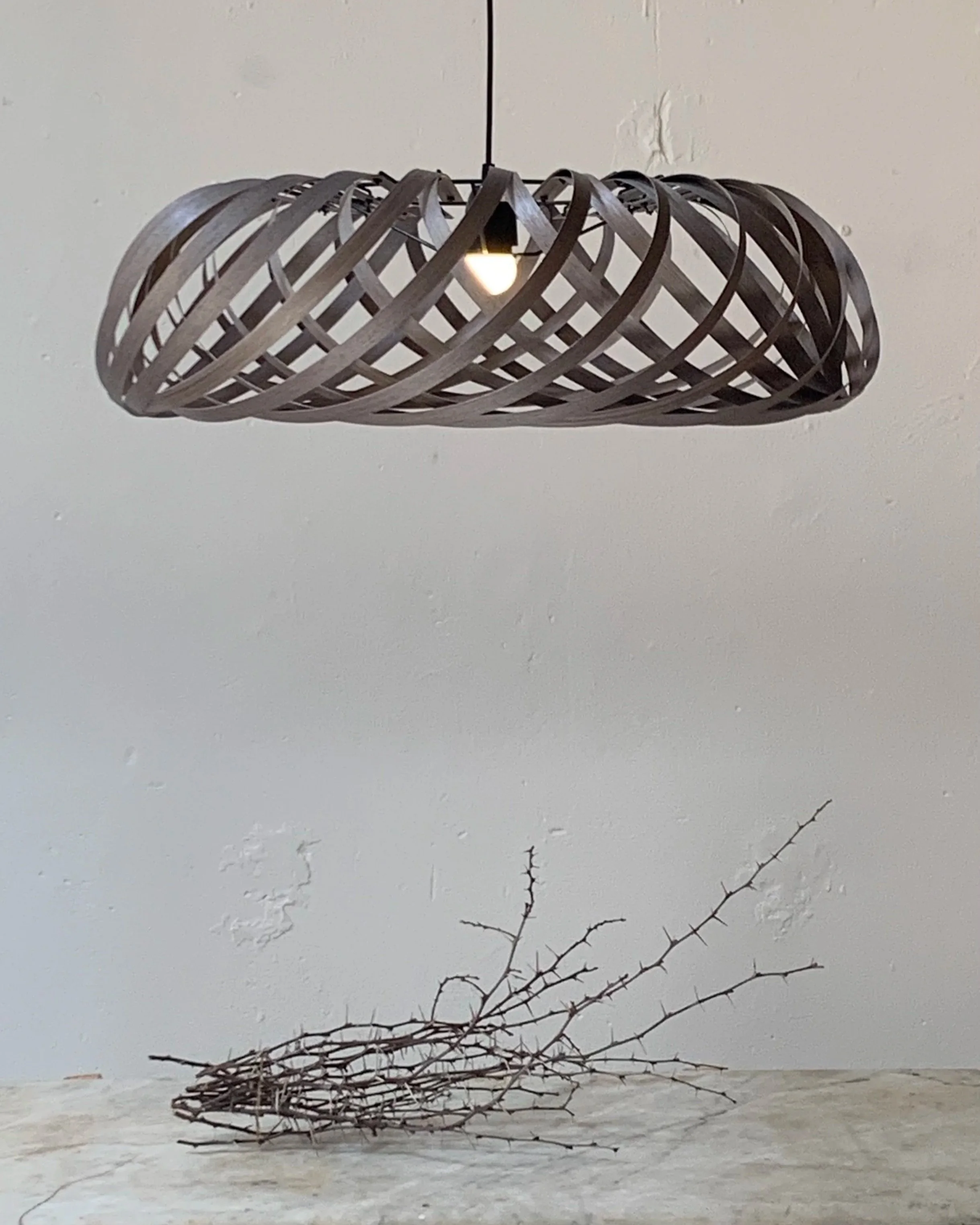 A hanging modern wooden light fixture above a table with a branch on it.