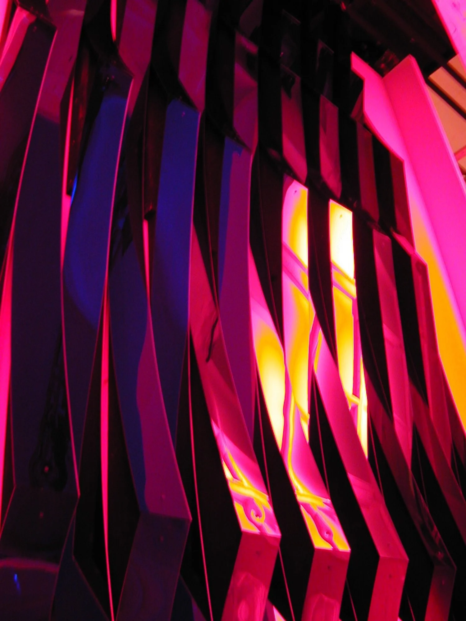 Colorful lighting with pink, purple, and yellow hues cast on wavy black and reflective surfaces.