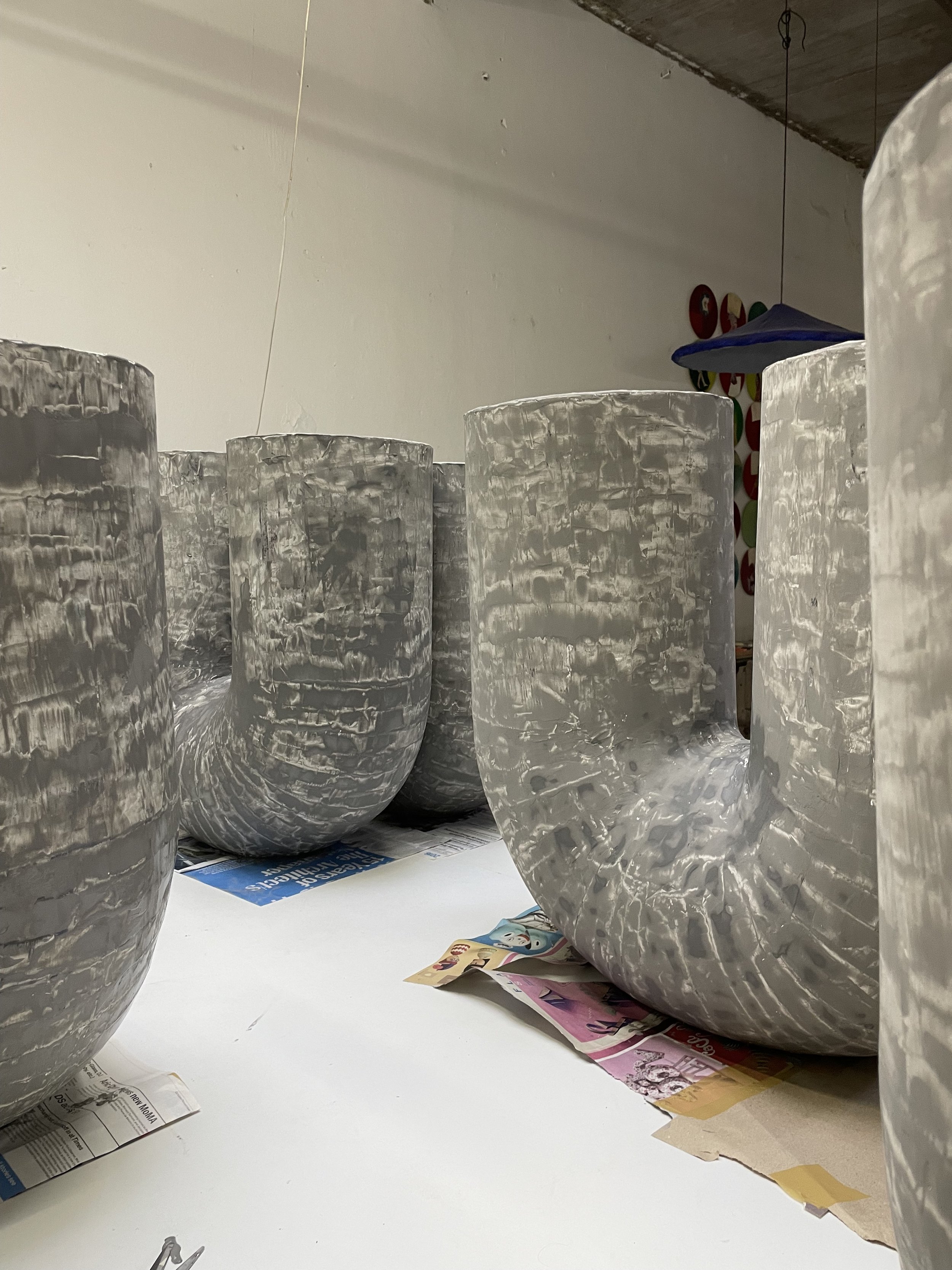 Several large, gray, textured planters with a marble-like finish arranged indoors, with magazines and newspapers on a white surface in the foreground.
