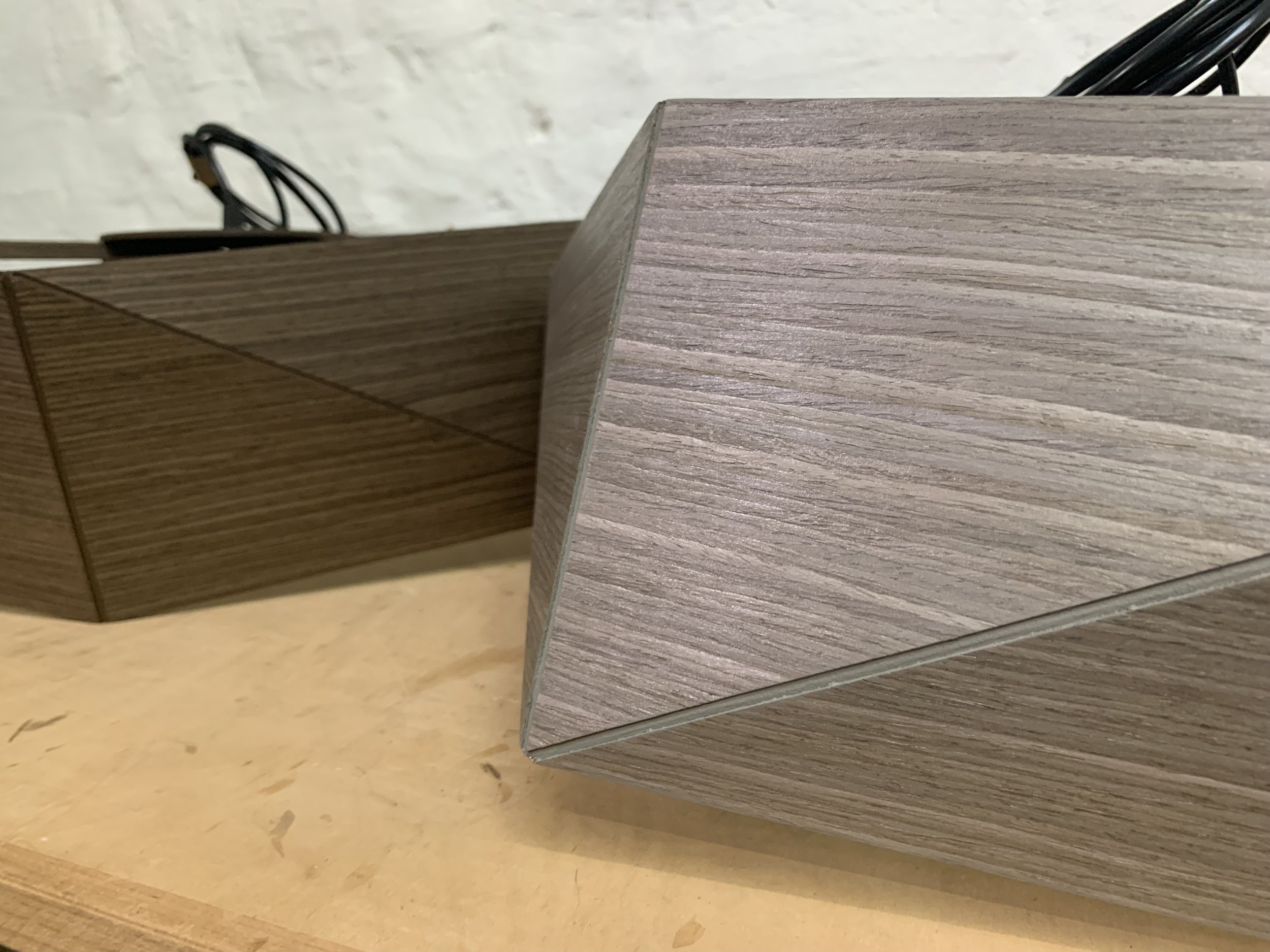 Close-up of two wooden geometric paperweights or decorative objects with different wood grain patterns placed on a wooden surface.