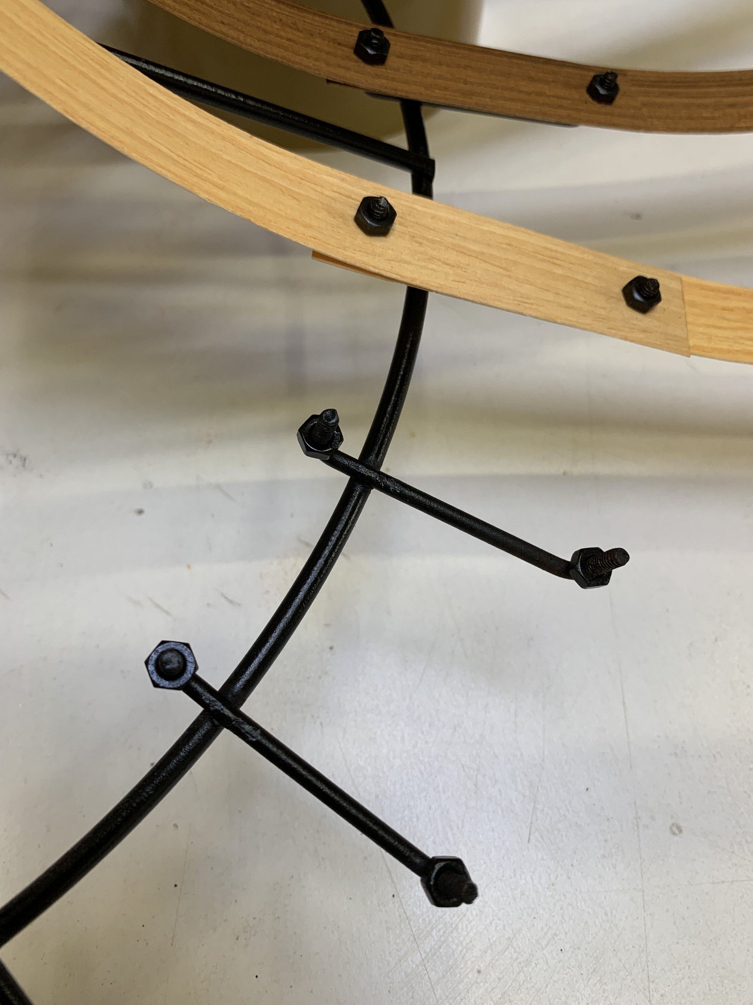 Close-up of a modern chair with a black metal base and wooden armrest, showing screws and structural elements.