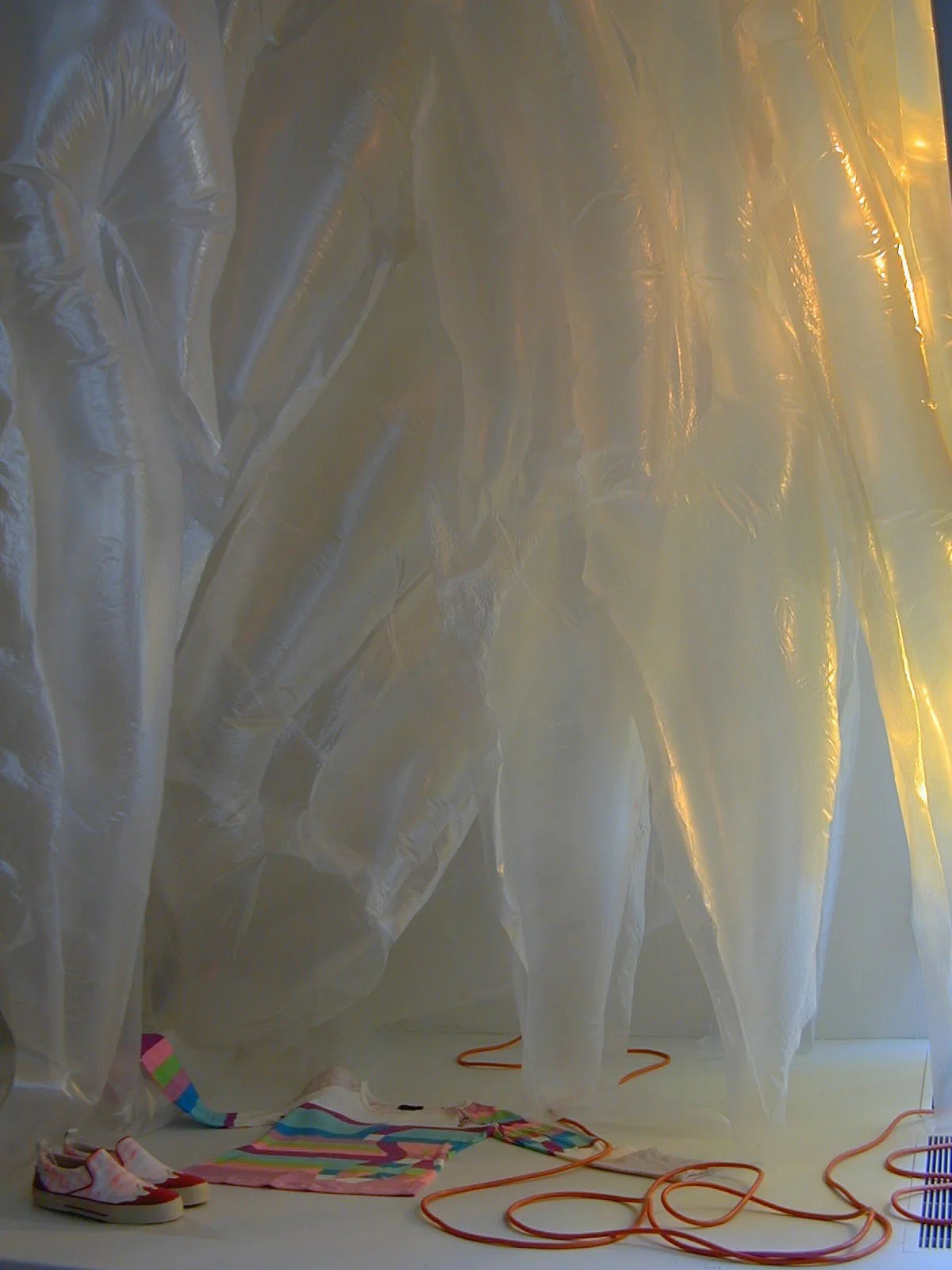 Plastic sheets and a pair of shoes on the floor, with orange extension cords and colorful fabric or towel.
