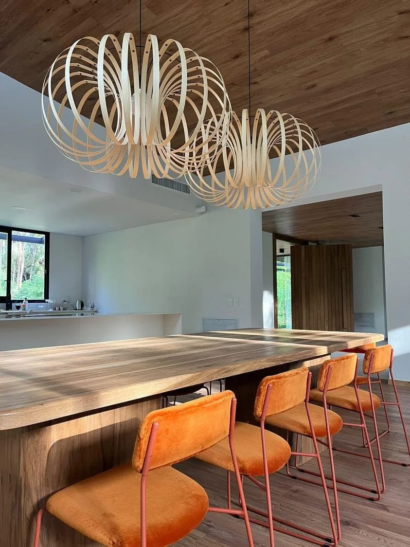 Modern dining area with a wooden table, orange velvet chairs, and a wooden pendant light fixture hanging from a wooden ceiling.
