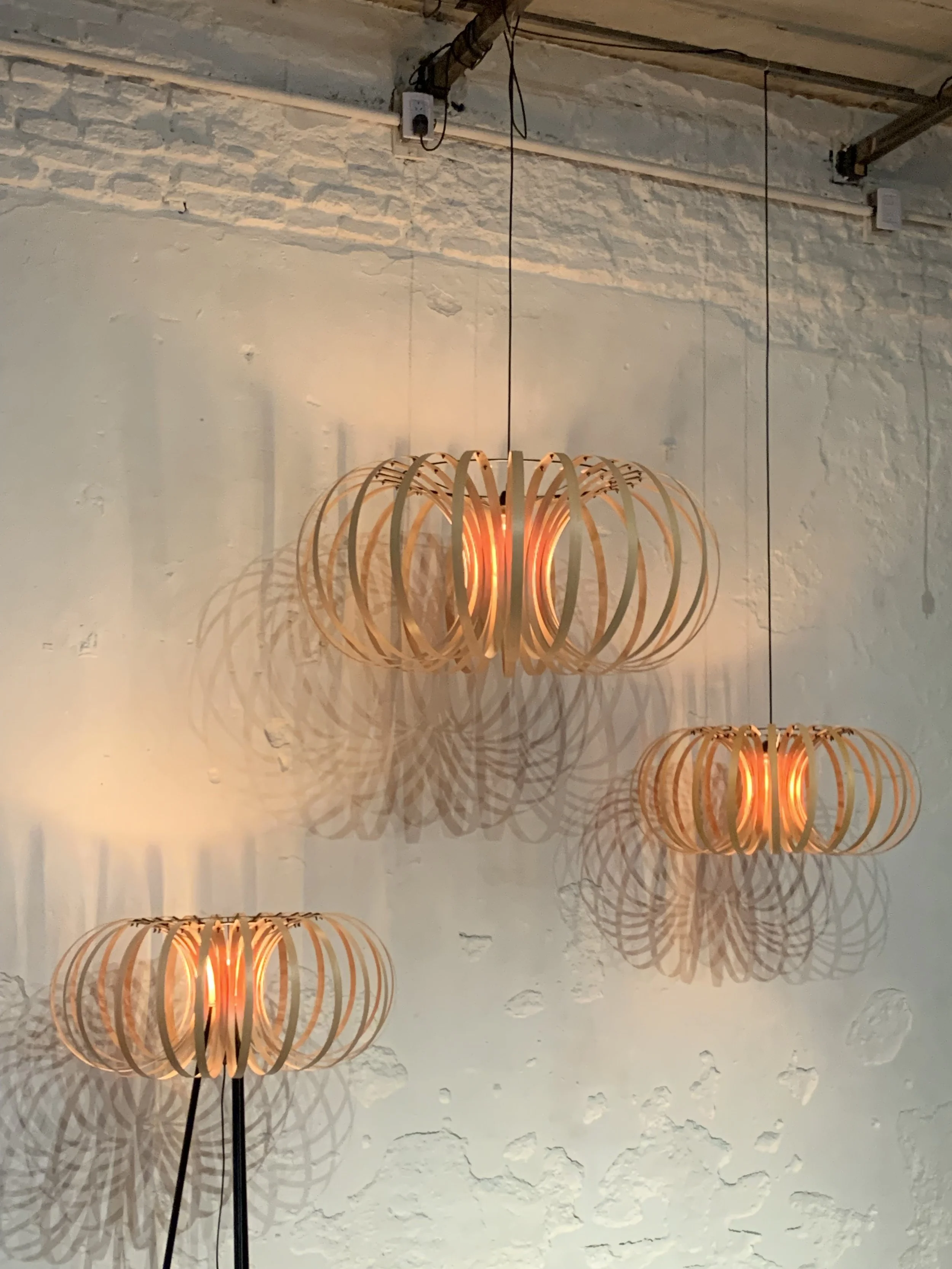 Three modern hanging pendant lights with wooden circular frames casting shadows on a white textured wall in an indoor space.