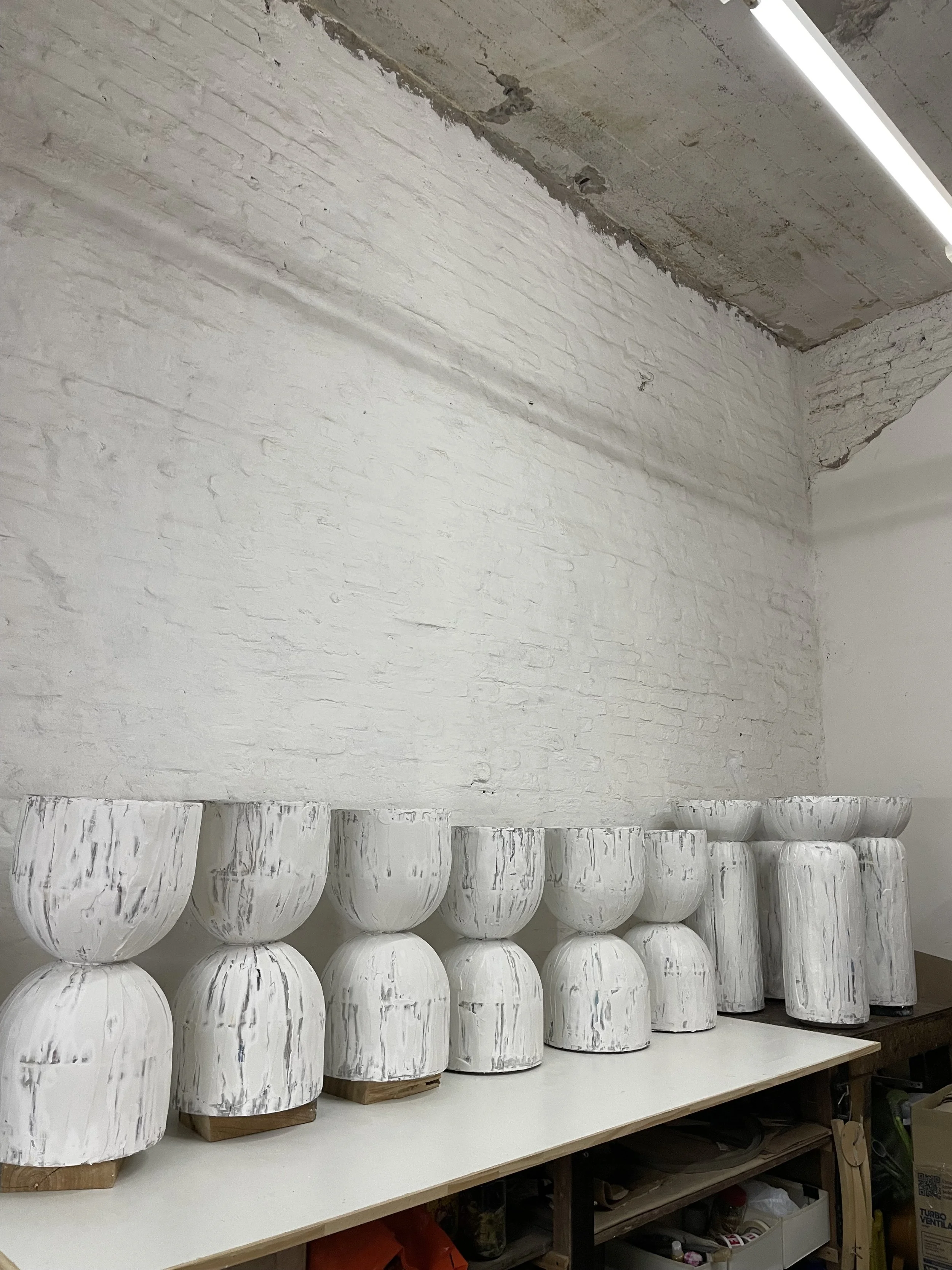 Several white moai-style sculptures with a distressed finish on a table against a white brick wall.