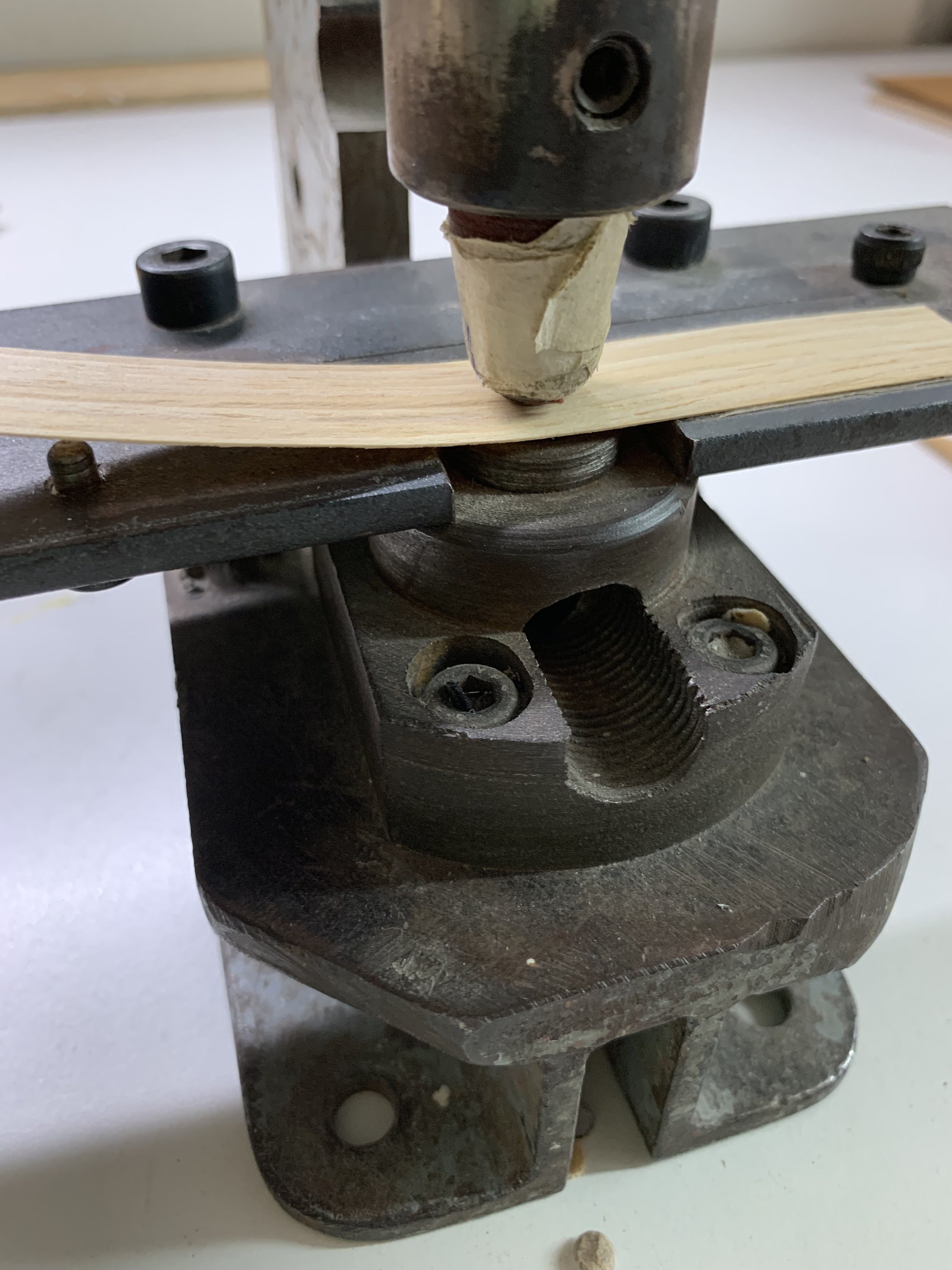 Close-up of a woodworking clamp holding a thin piece of wood in place on a workbench.