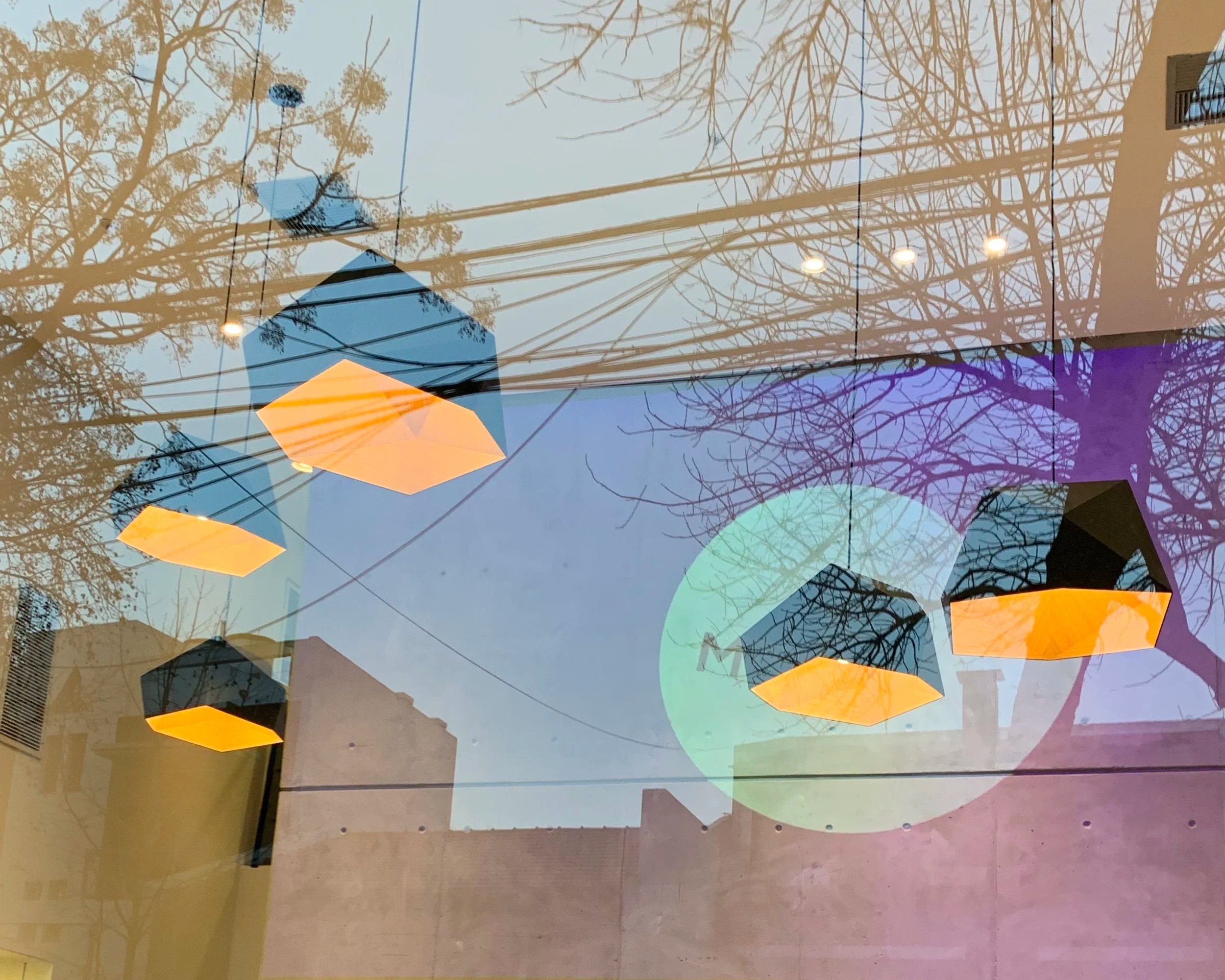 Reflection of leafless trees and power lines on a glass window with three hanging geometric pendant lights glowing yellow.