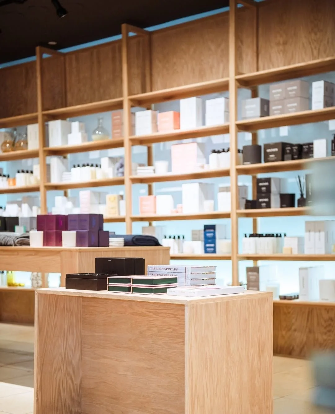 View of retail store with wooden shelving filled with various boxes and packaging, and a wooden table in the foreground displaying boxed products.