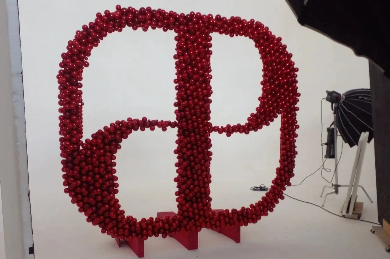 A large wall decoration of the letter 'P' made from red ornaments in a studio with photography equipment.