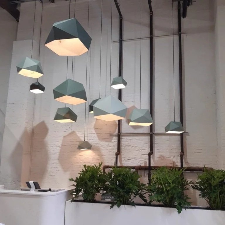 Modern hanging pendant lights above a reception desk with green plants in front, against a white brick wall.
