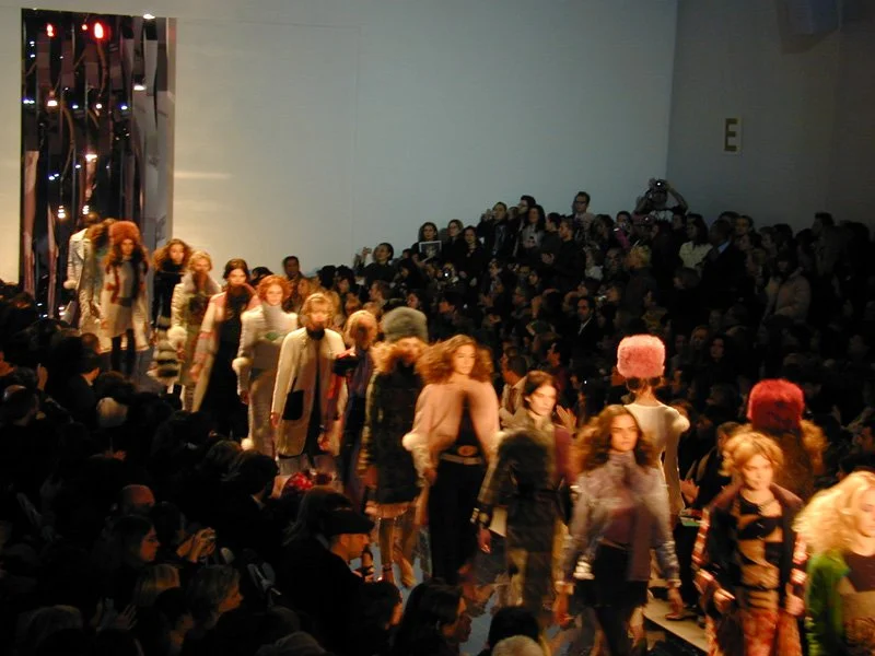 Models walking down the runway at a fashion show with an audience watching.