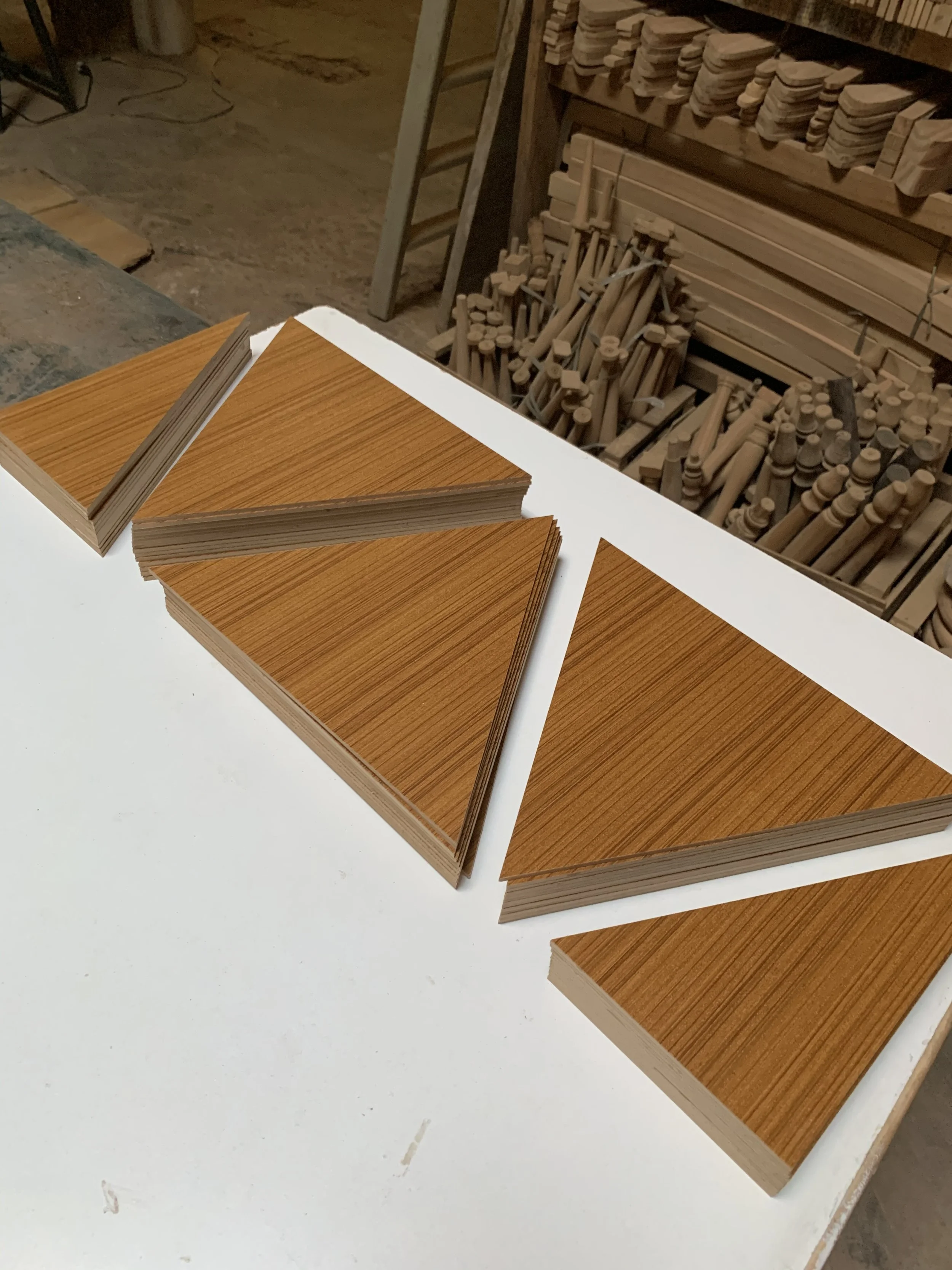 Stacks of wood veneer sheets with a wood grain pattern on a white surface in a woodworking shop.