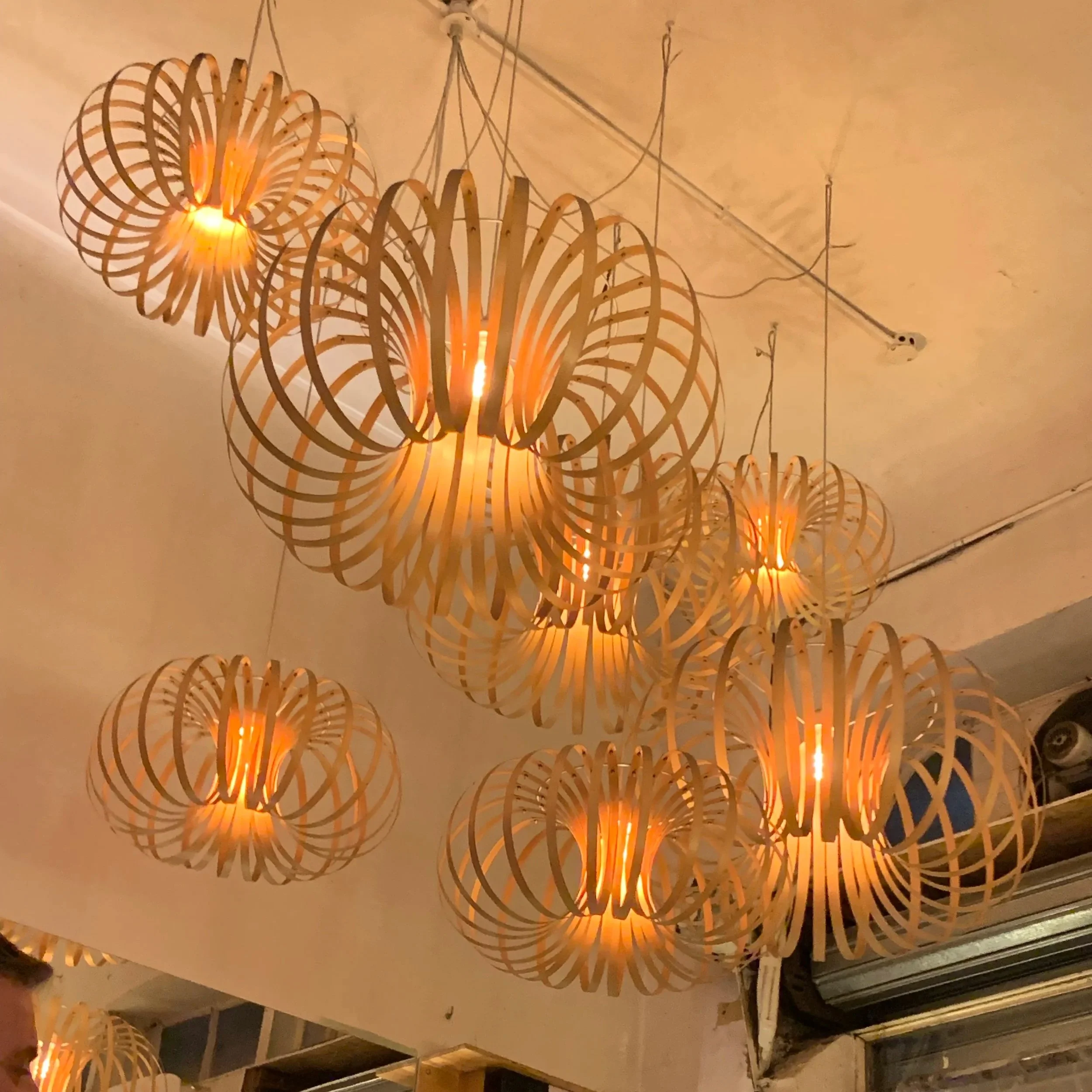 A group of decorative hanging light fixtures made of wood in a spherical, open-lattice design, emitting warm light, mounted on a ceiling.