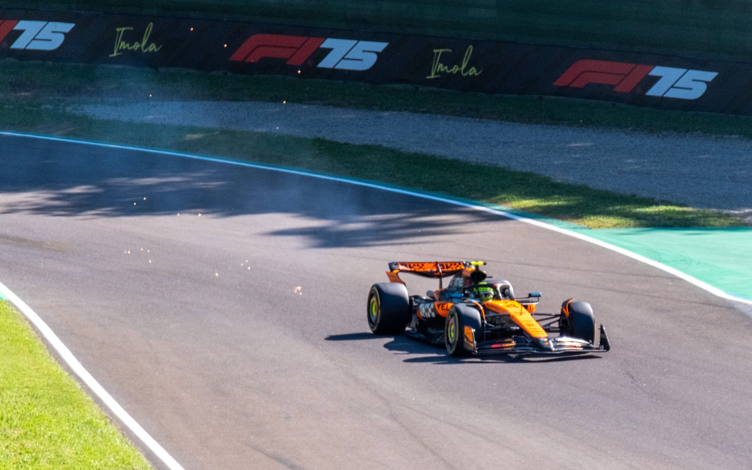 A Formula 1 car on a racetrack with sponsorship and branding visible, including 'Imola' and 'F1 75' signs.