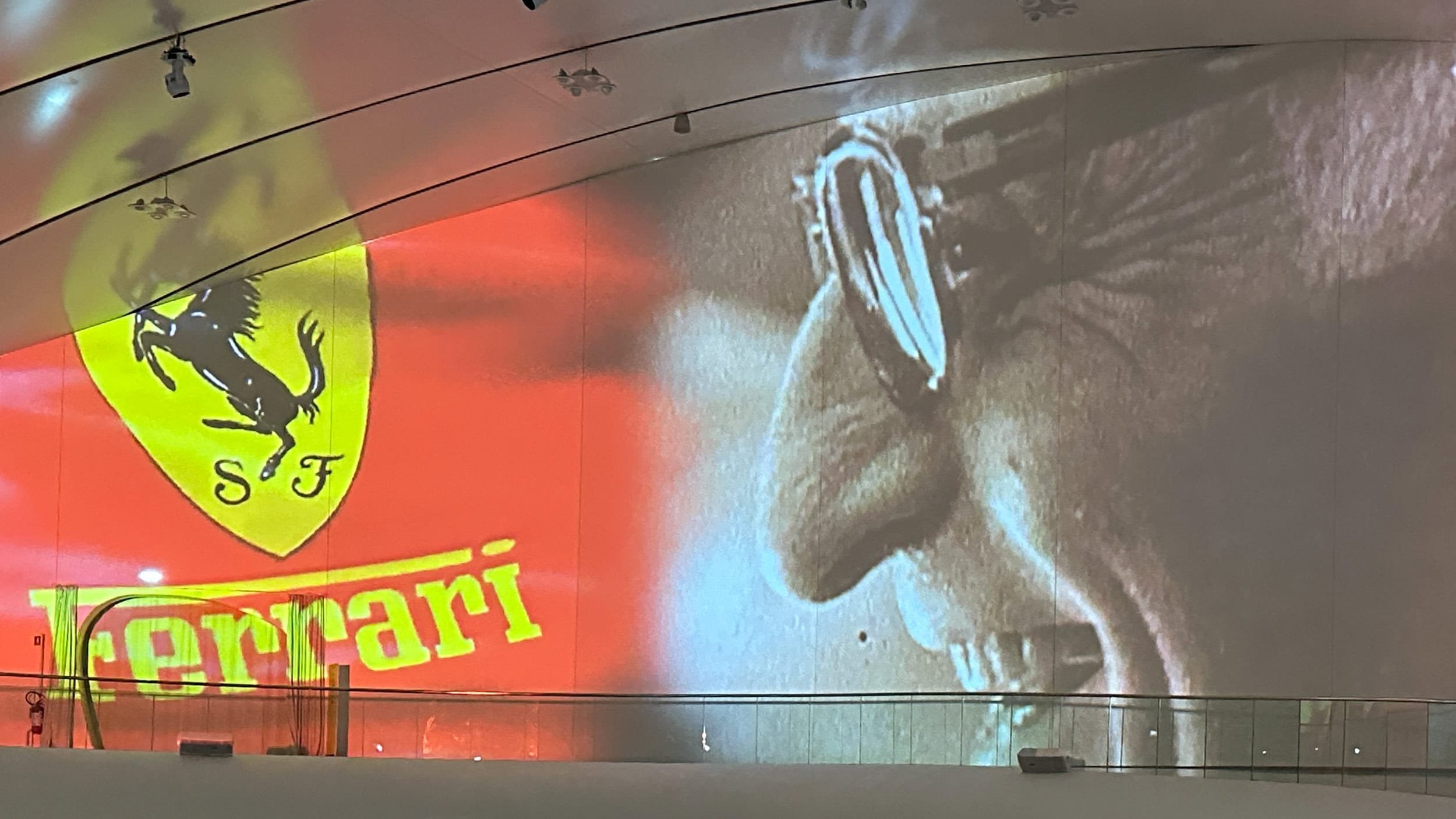 Large Ferrari projection display inside the Enzo Ferrari Museum in Modena, Italy, featuring the Ferrari logo alongside a black-and-white portrait of Enzo Ferrari wearing sunglasses.