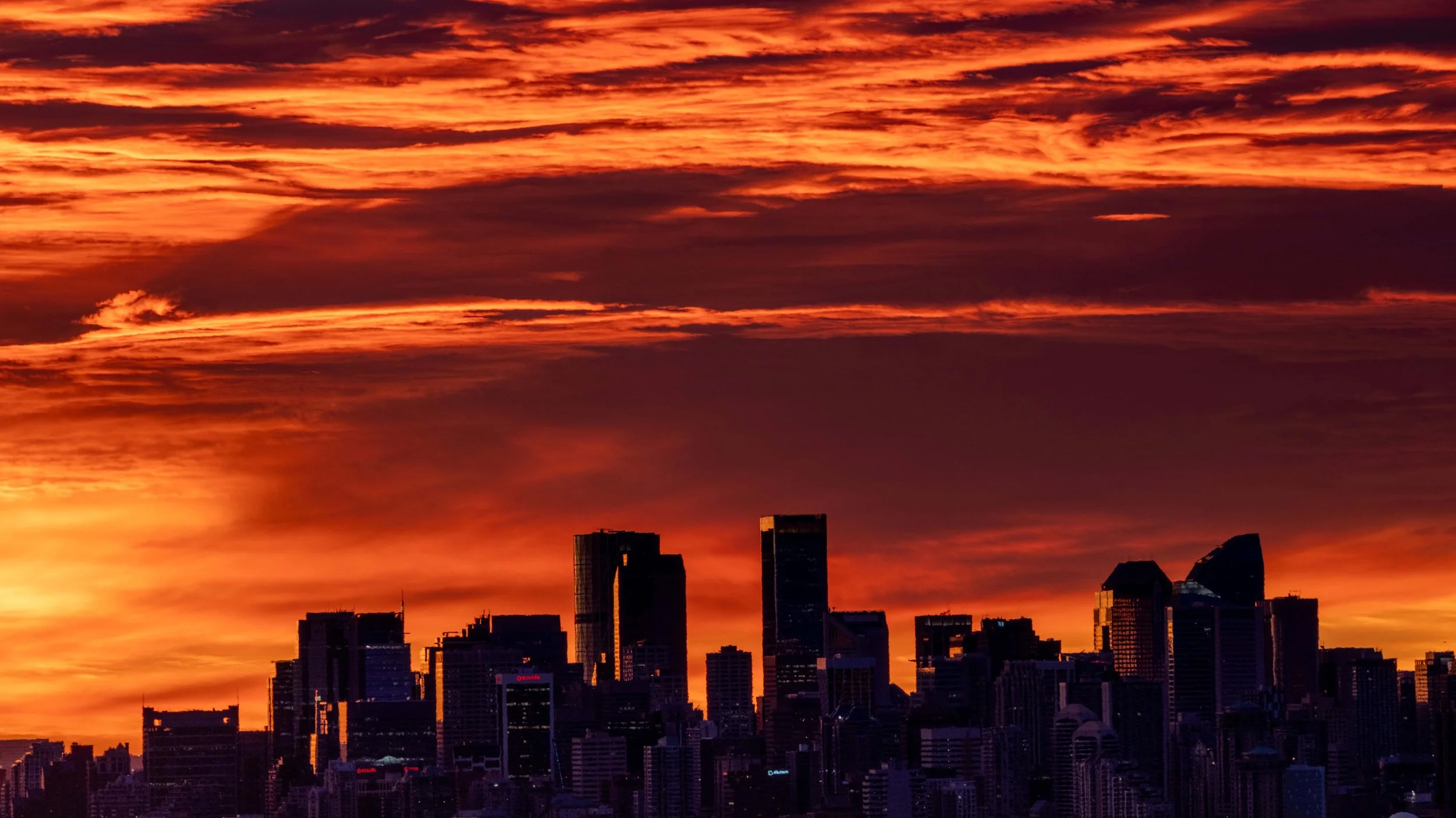 Silhouetted Calgary skyline with fiery sunrise sky, skyscrapers outlined against vibrant orange and red clouds.