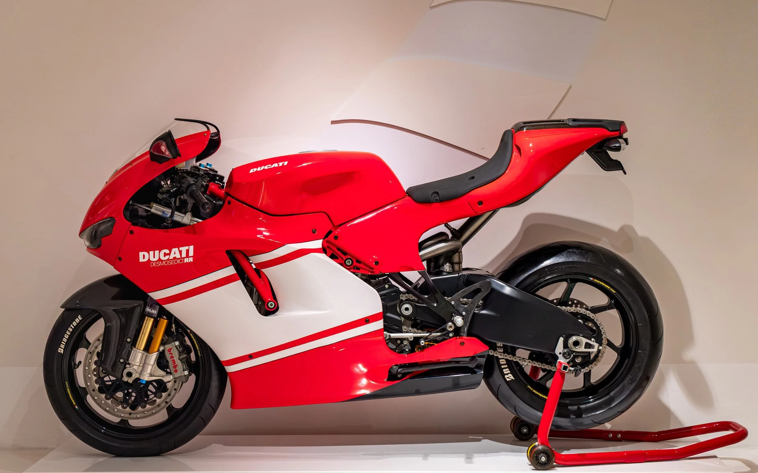 Side profile of a Ducati Desmosedici RR superbike displayed at the Ducati Museum in Bologna, Italy, showcasing its MotoGP-inspired design, racing slick tires, aerodynamic fairings, and iconic red Ducati styling.