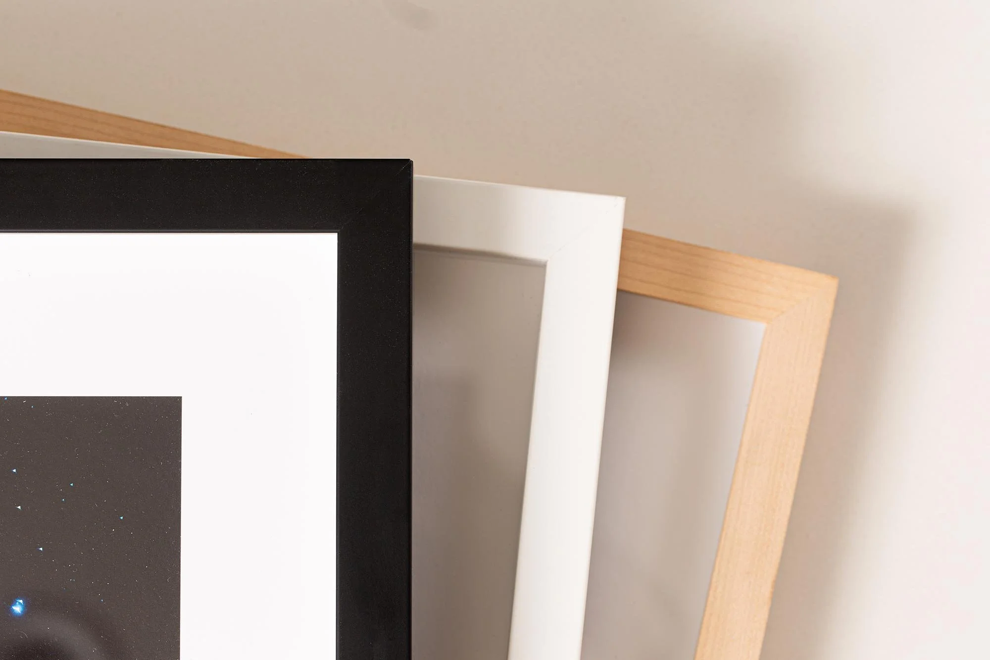 Close-up of three framed pictures leaning against a wall, with black, white, and light wood-colored frames.