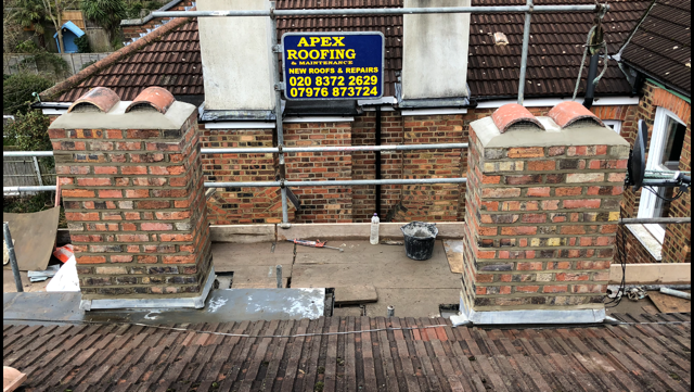 View of a rooftop under construction with two brick chimney structures, scaffolding, and a sign for Apex Roofing & Maintenance on the wall behind.