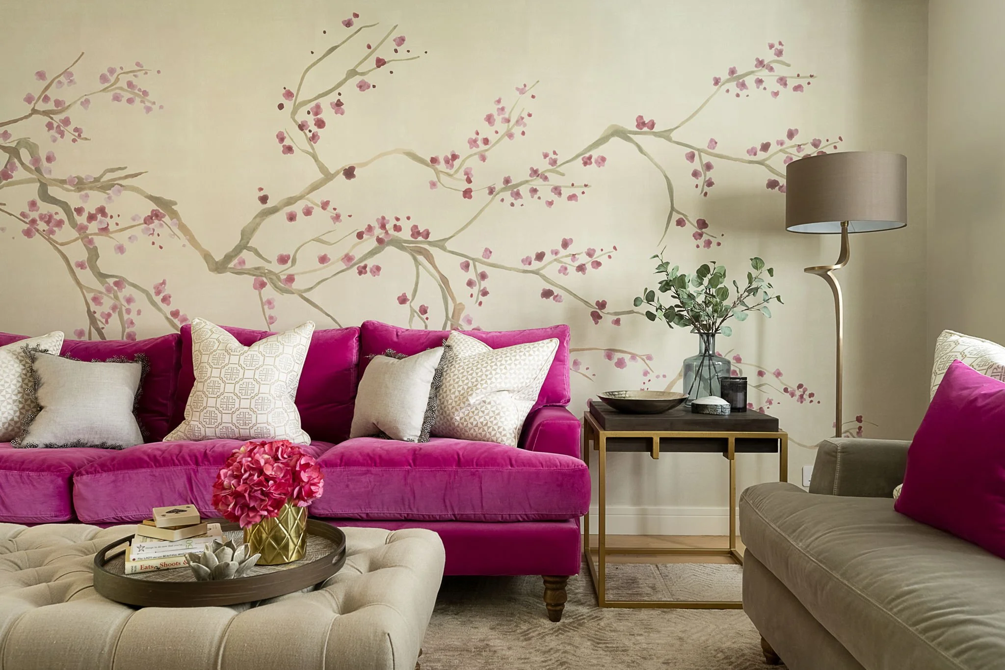 Warm neutral living room with a vibrant pink velvet sofa and delicate blossom mural, designed by Holly Scott Interior Design in Oxfordshire.