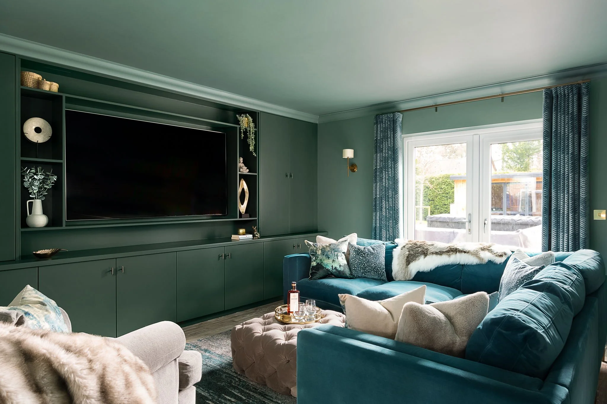Green colour-drenched living room with matching walls and bespoke built-in cabinetry, teal velvet sofa and layered textures, designed by Holly Scott Interior Design in Oxfordshire.