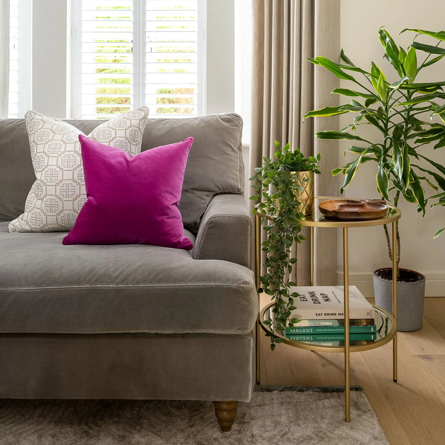 Warm neutral living room with grey velvet sofa, natural curtains, greenery and a vibrant pink cushion, designed by Holly Scott Interior Design in Oxfordshire.